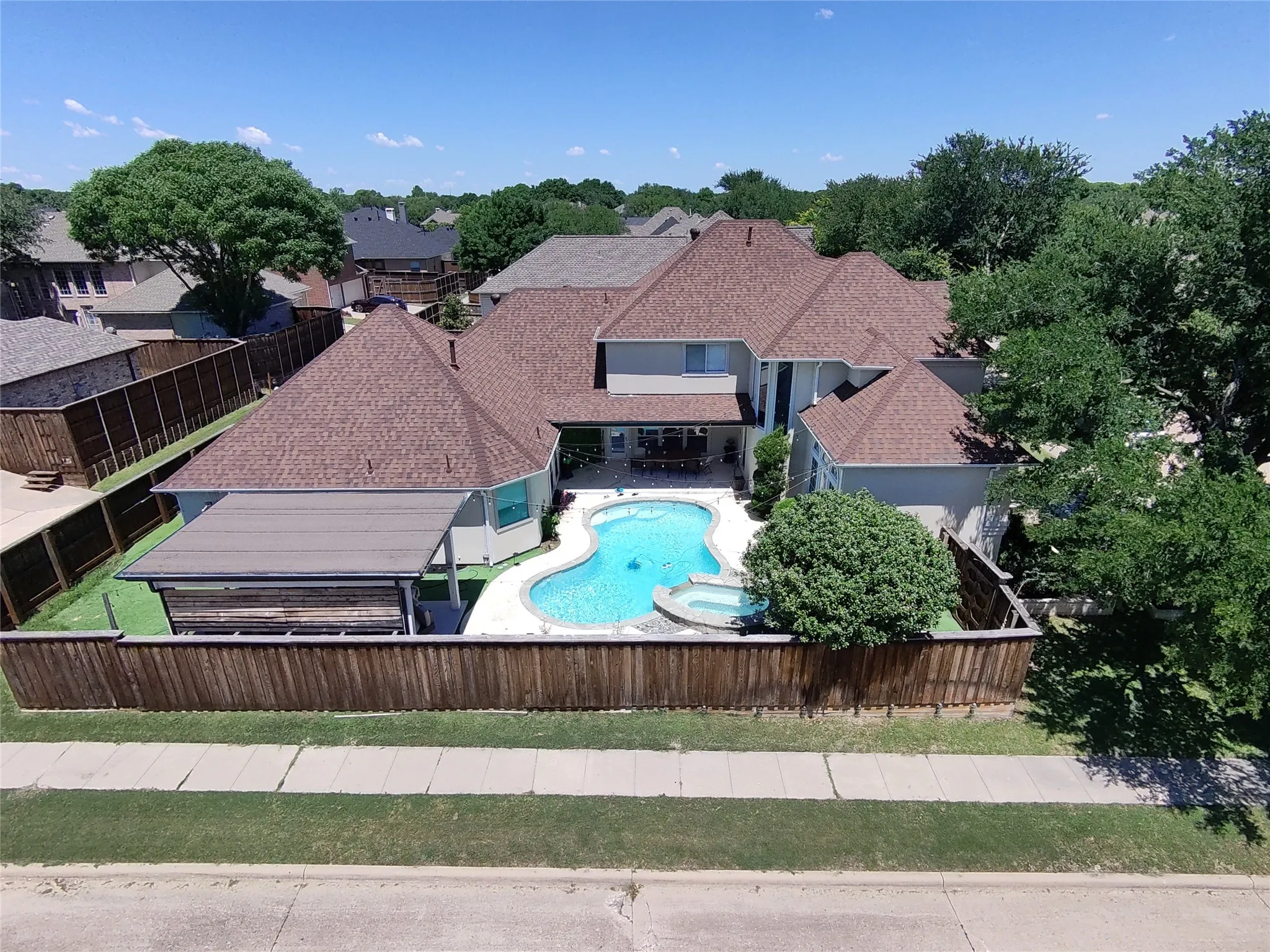 Backyard oasis featuring a curvilinear swimming pool with integrated spa, covered patio, and manicured turf surrounding the pool deck
