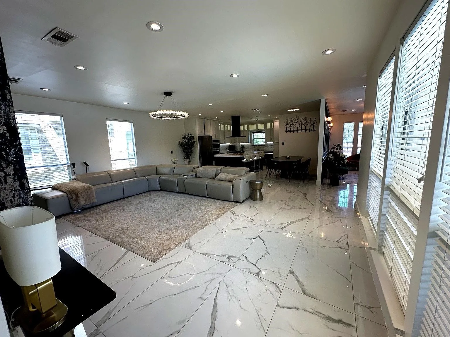 Spacious open-concept living area featuring large format marble-look tile flooring, recessed lighting, and multiple windows with horizontal blinds