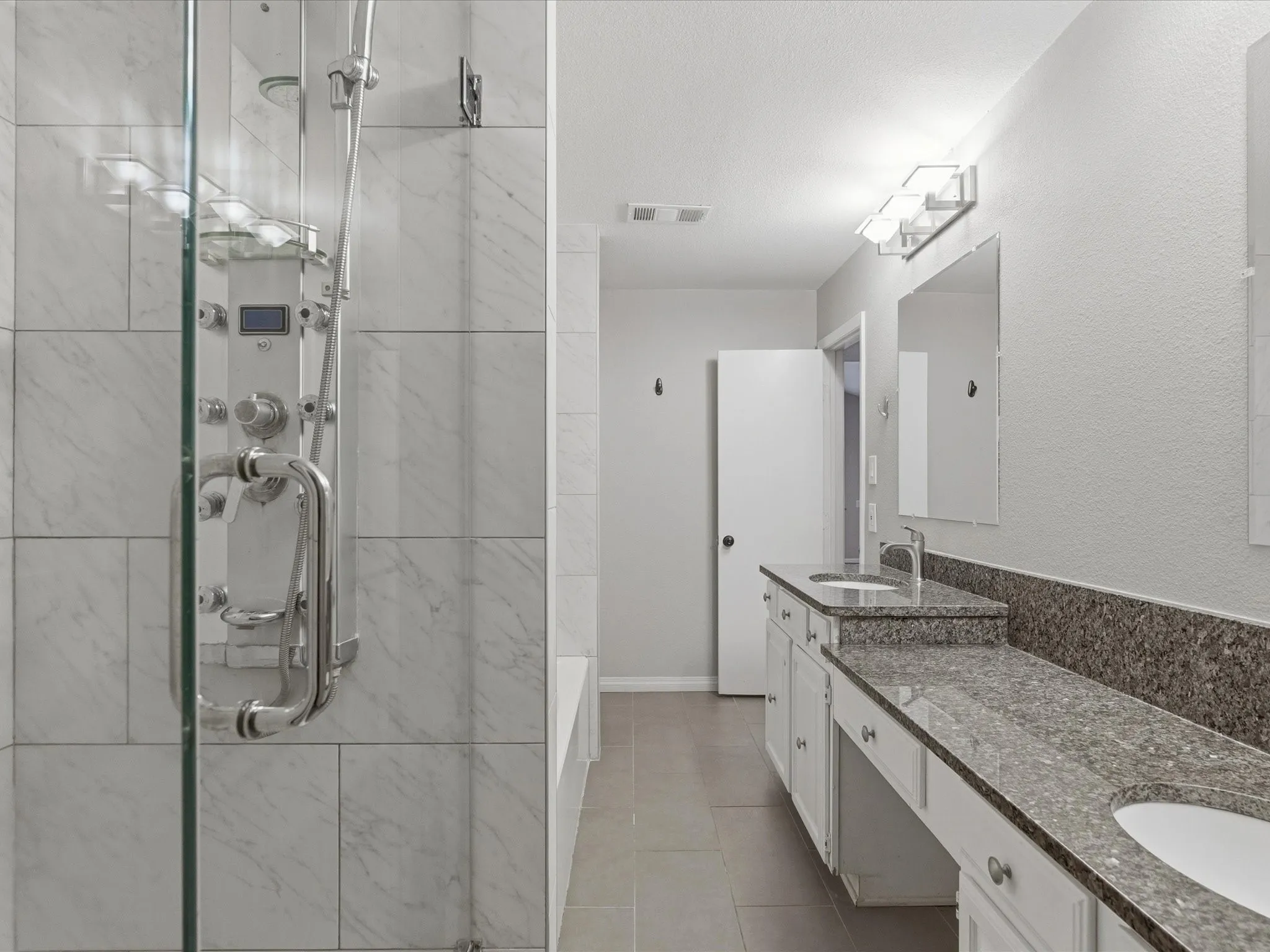 Glass-enclosed shower with wall-mounted shower panel and light-toned tile surround