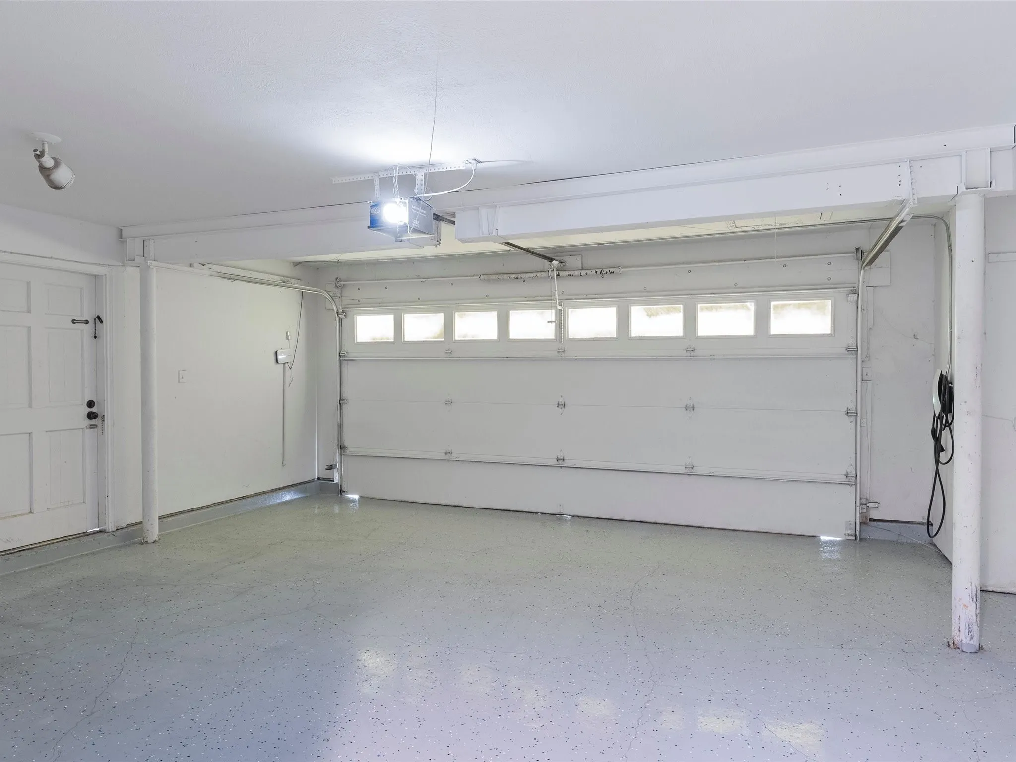 Two-car garage featuring an automatic garage door opener, overhead lighting, side pedestrian door, and a light gray speckled epoxy-coated floor