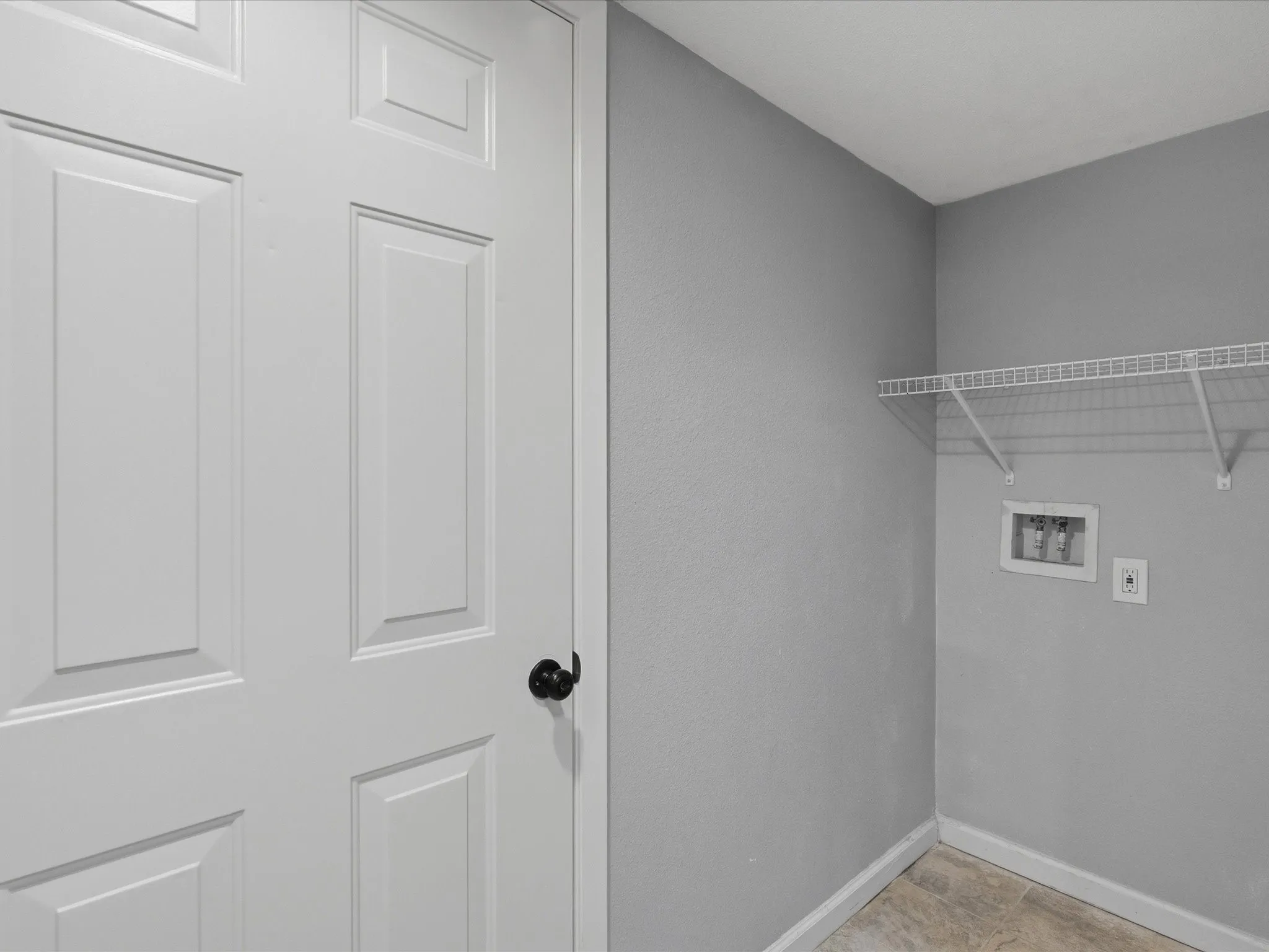 Utility space featuring light gray walls, wire shelving, and tile-finish flooring
