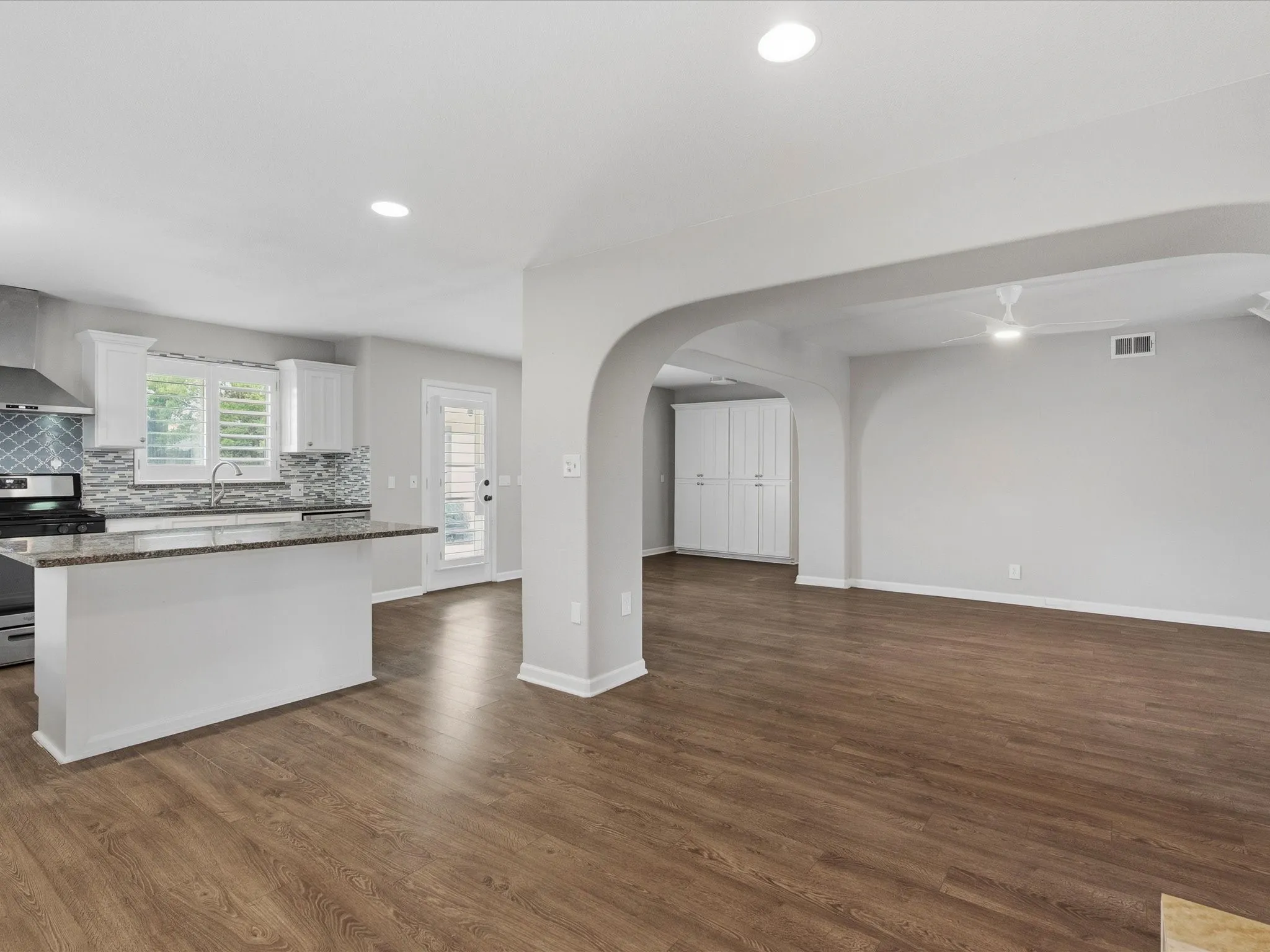Open-concept living space featuring wood-finish flooring, recessed lighting, and an arched entryway