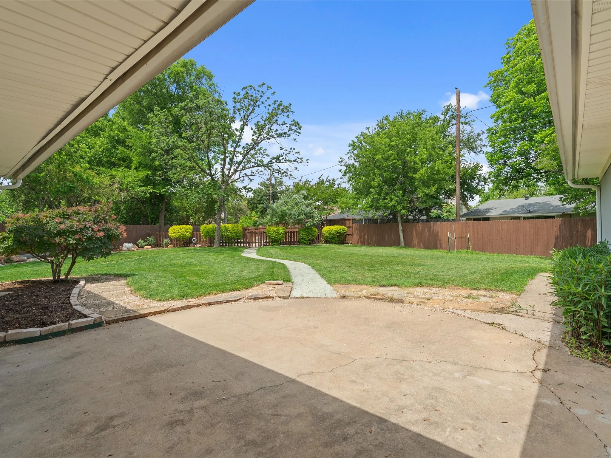 Spacious backyard featuring a concrete patio, a winding stone pathway, a manicured lawn, and mature privacy fencing