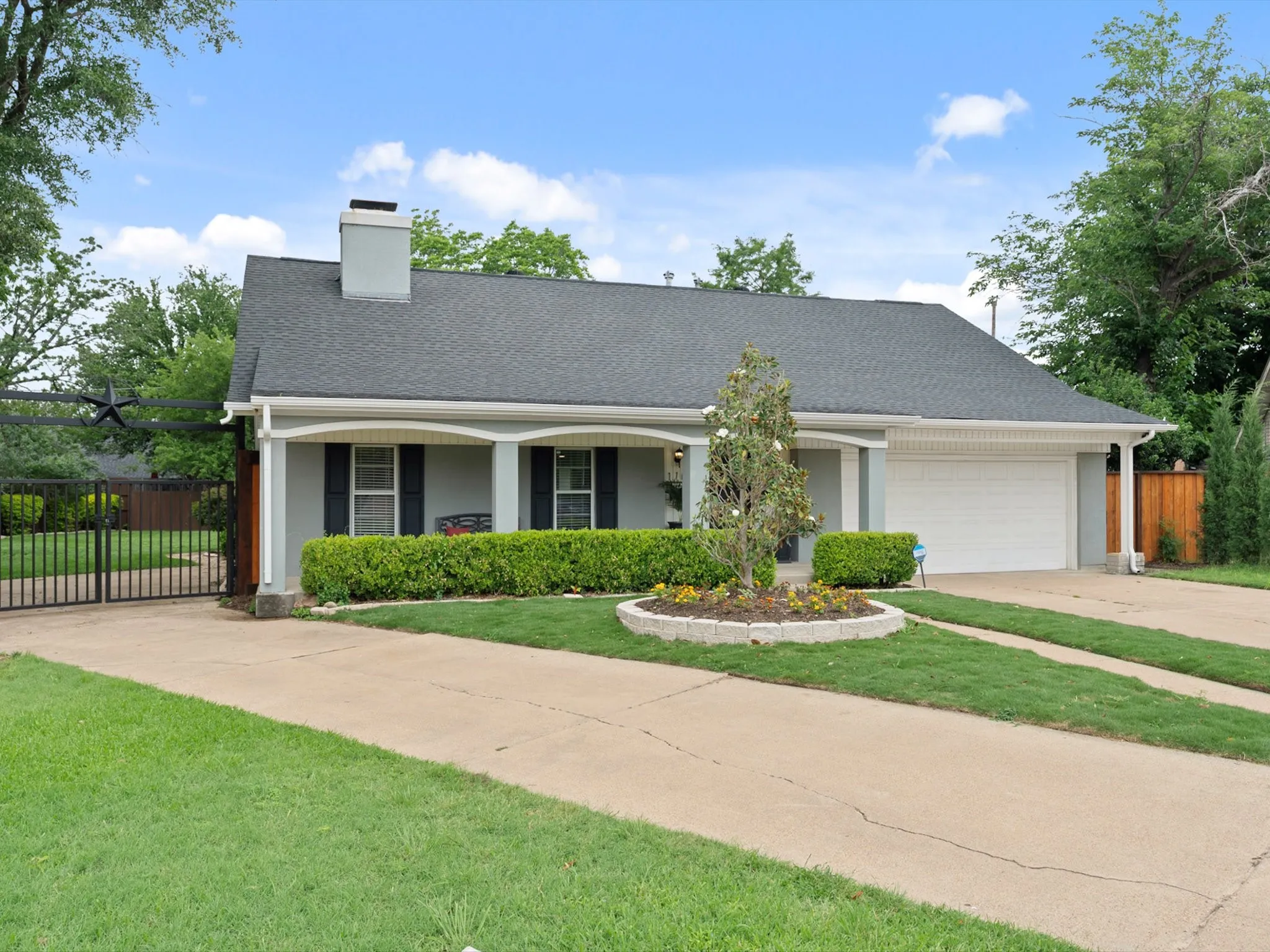 Single-story residence featuring a gray exterior with a dark shingle roof, an attached two-car garage, and a gated driveway entry