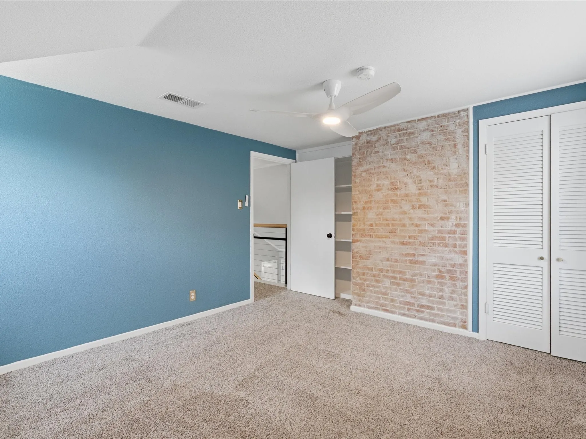 Bedroom featuring plush carpet flooring, a ceiling fan with integrated lighting, and a prominent exposed brick accent wall