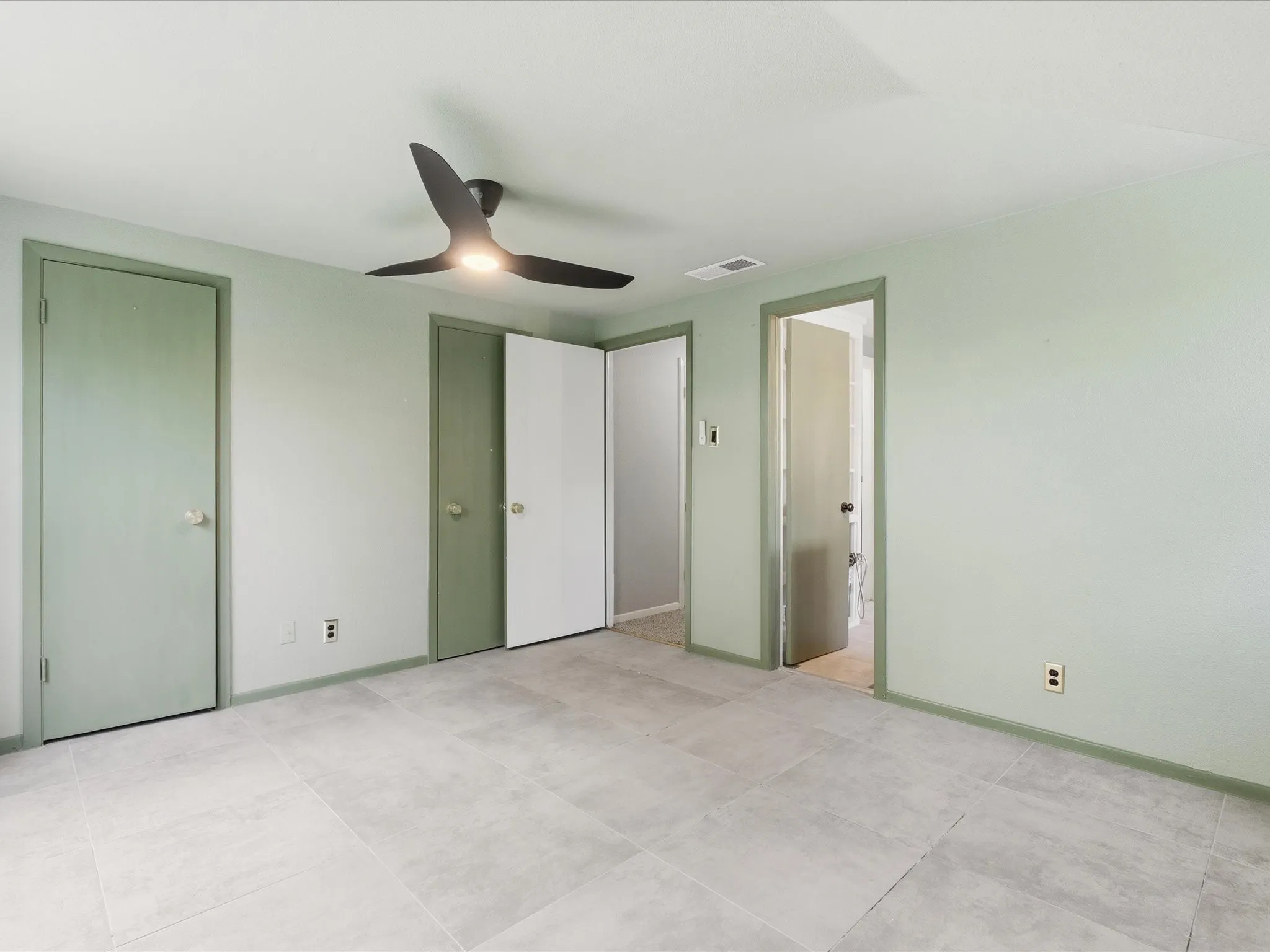 Spacious interior room featuring light-toned tile flooring, light green walls with matching trim, and a contemporary ceiling fan with integrated lighting