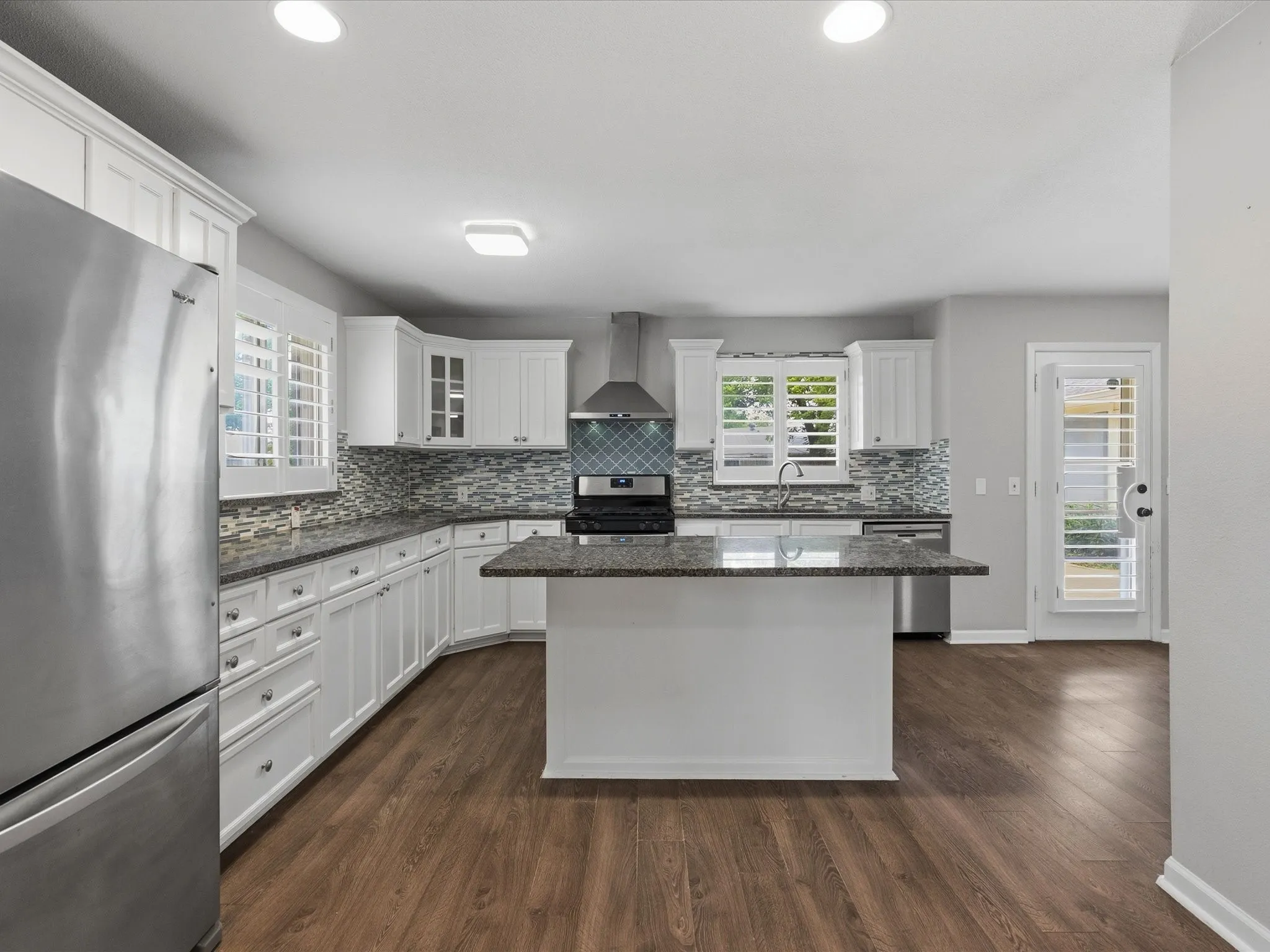 Modern kitchen featuring white cabinetry, a central island with a granite countertop, and wood-finish flooring