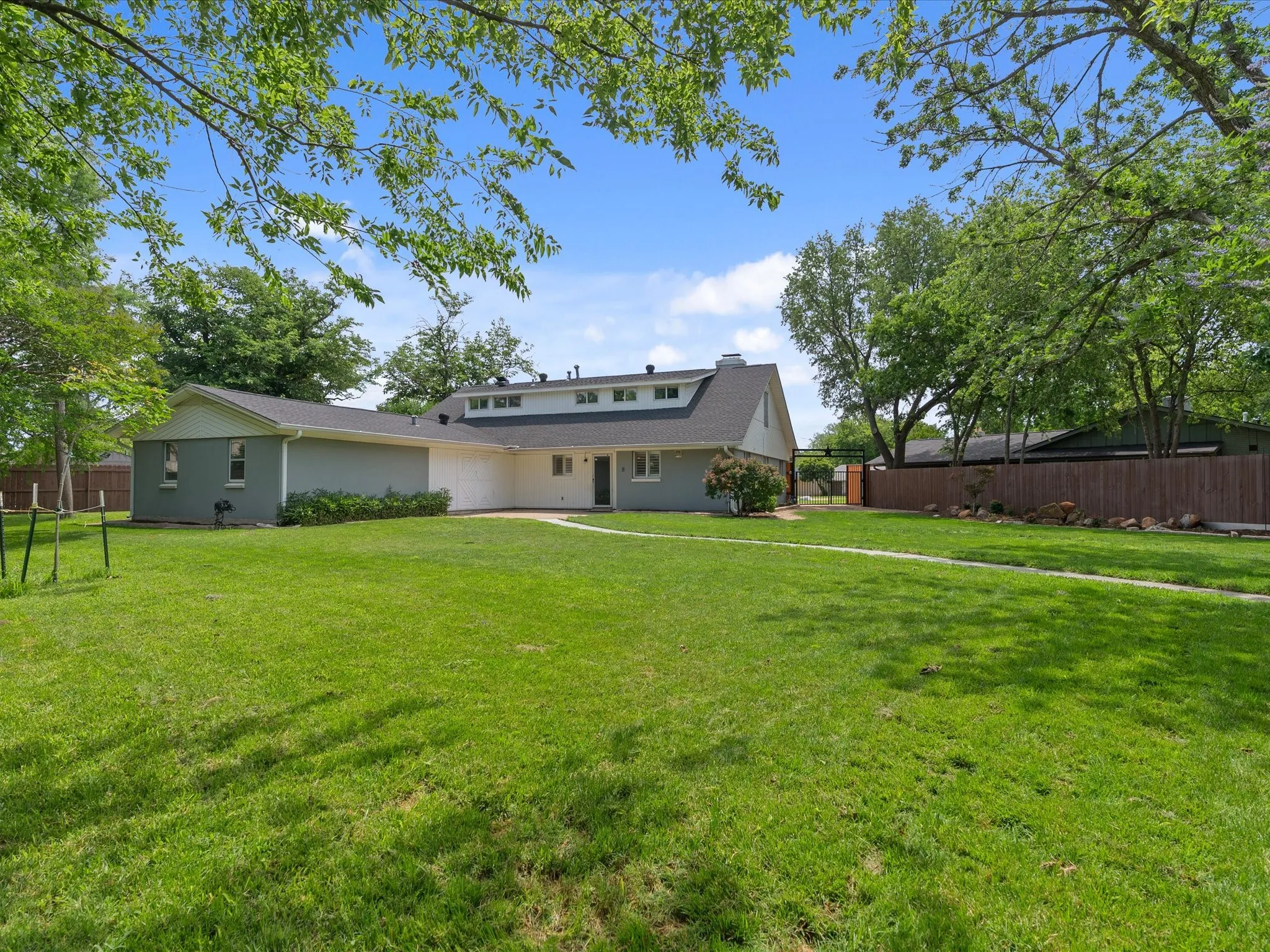 Expansive green lawn surrounds a single-story residence featuring a gray exterior, white trim, and a dark shingle roof
