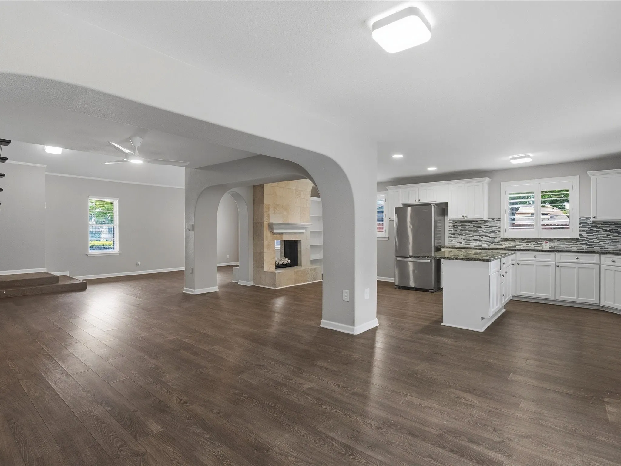 Open-concept living space featuring wood-finish flooring, a stone-clad fireplace with mantel, and arched doorways
