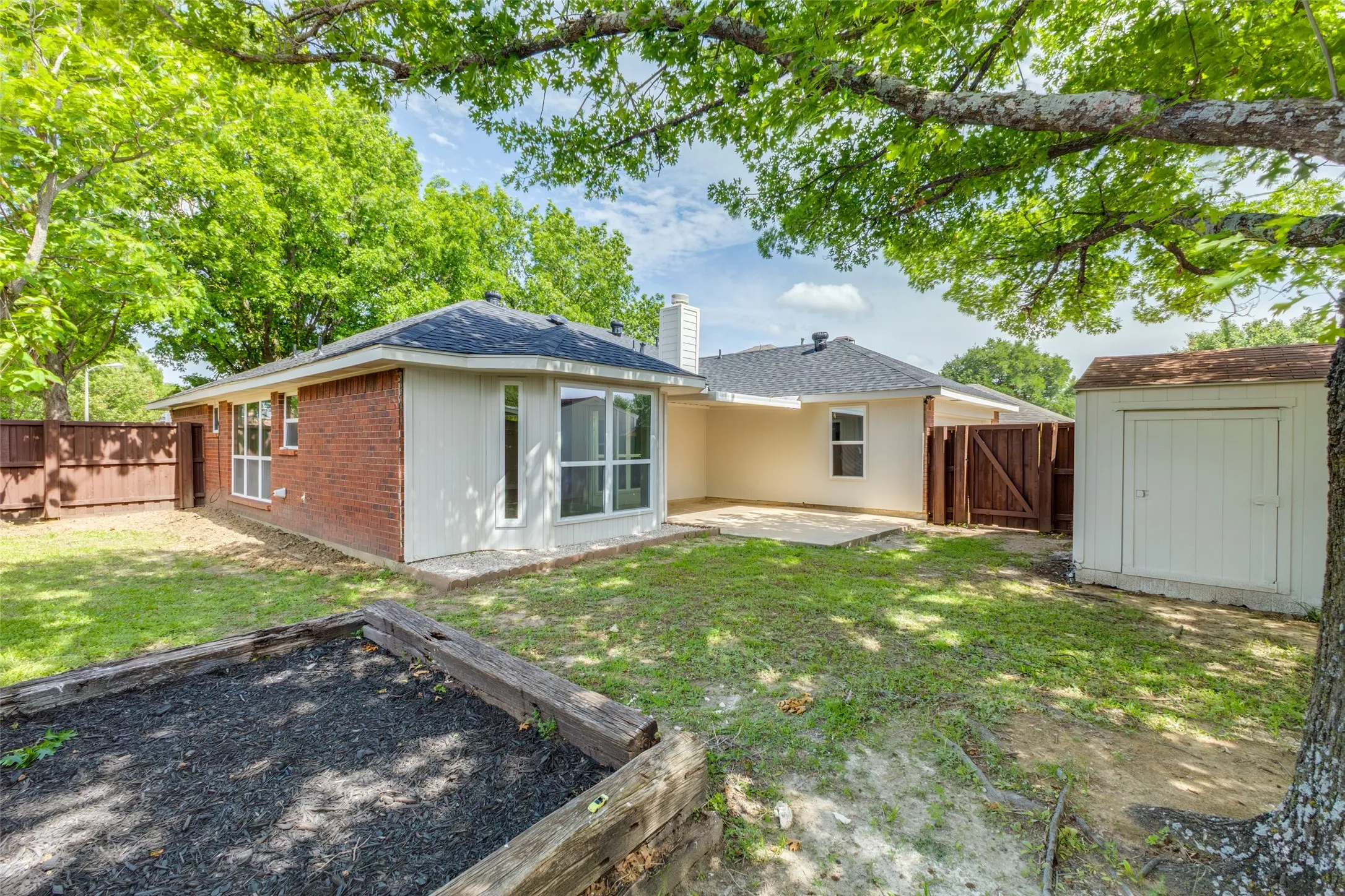 Expansive backyard featuring a brick and siding exterior, a concrete patio, a privacy fence, a storage shed, and a raised garden bed