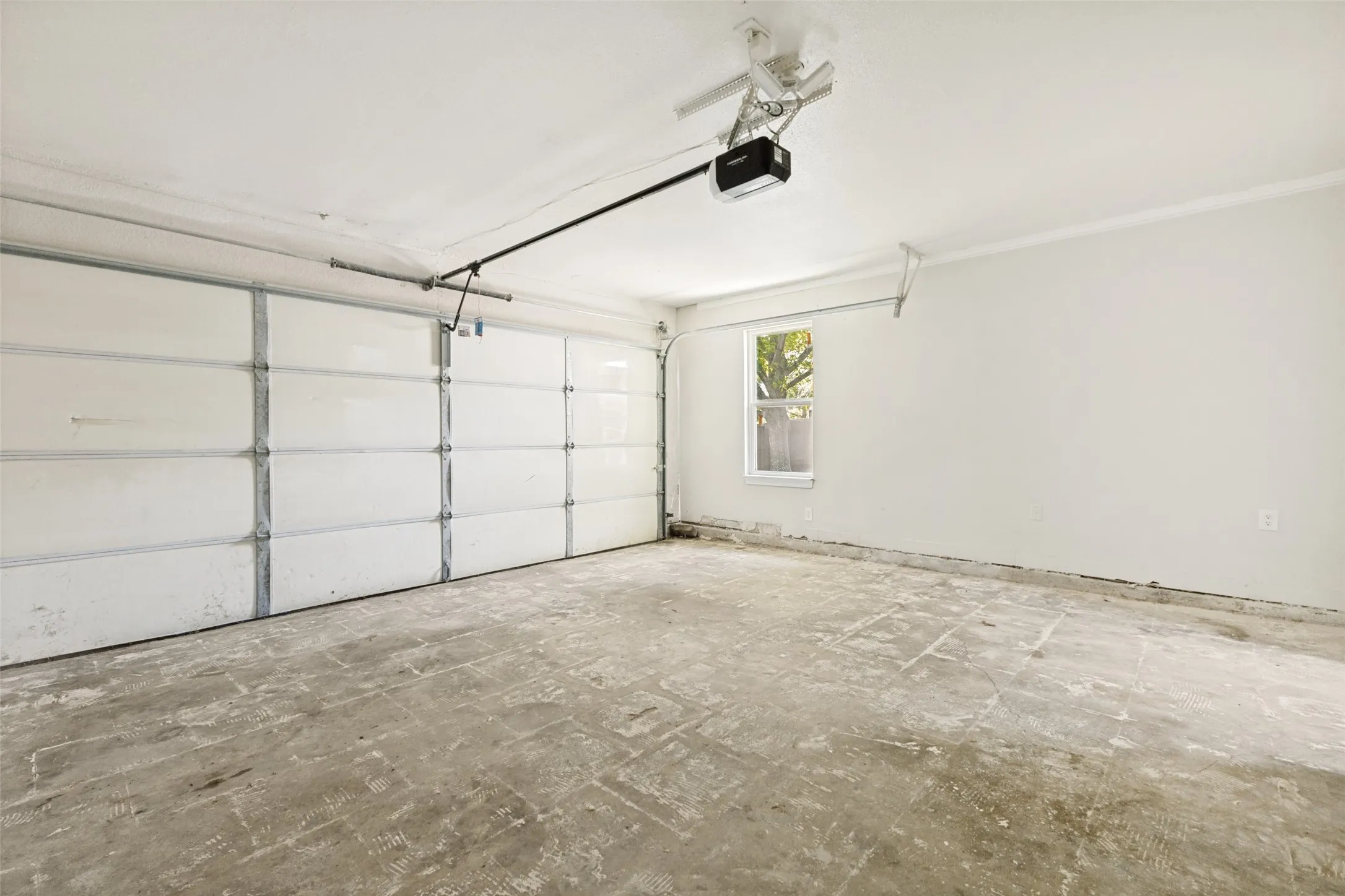 Spacious garage featuring a paneled overhead door, an automatic opener, a single window, and concrete flooring