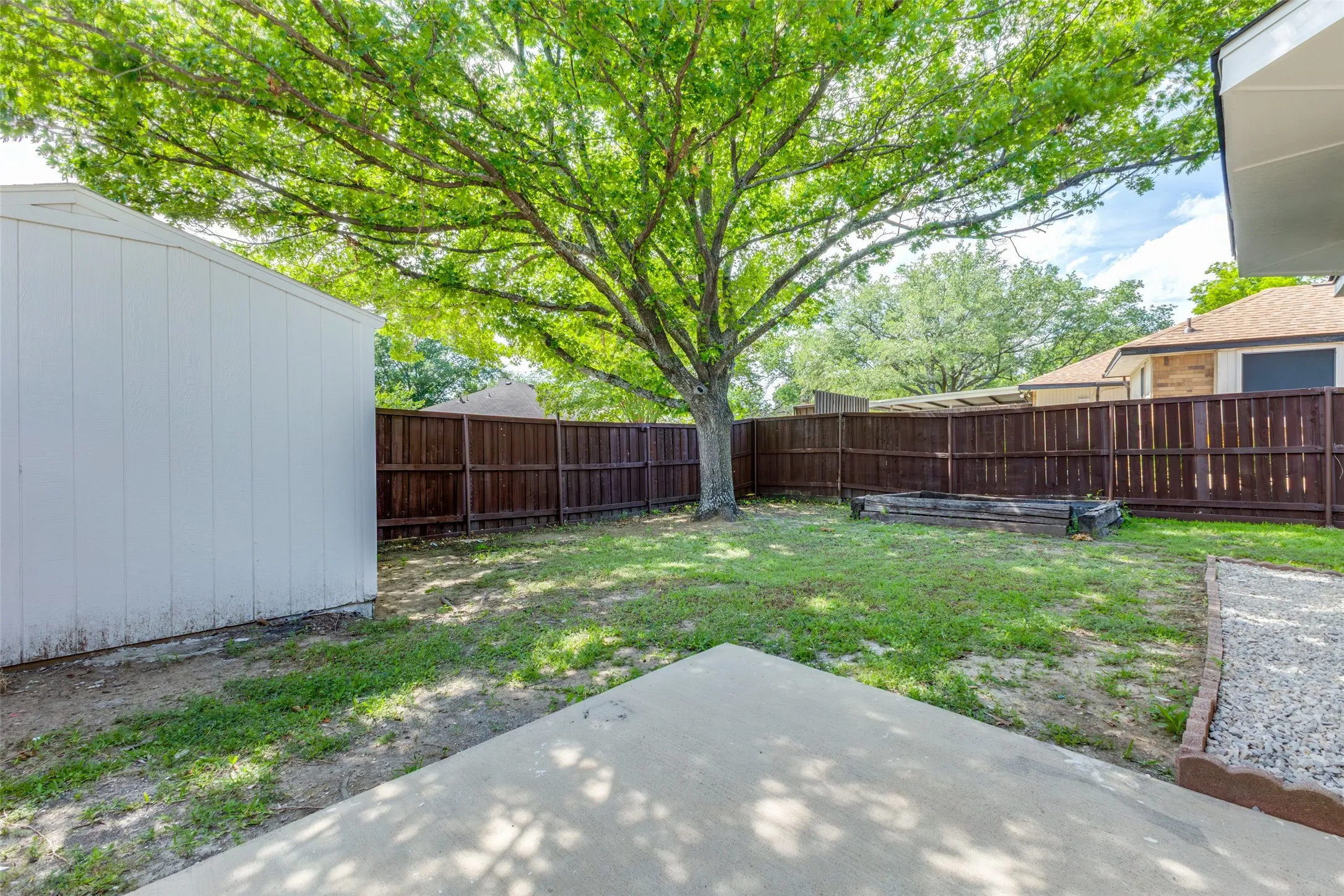 Expansive backyard featuring a mature shade tree, a white storage shed, and a privacy fence