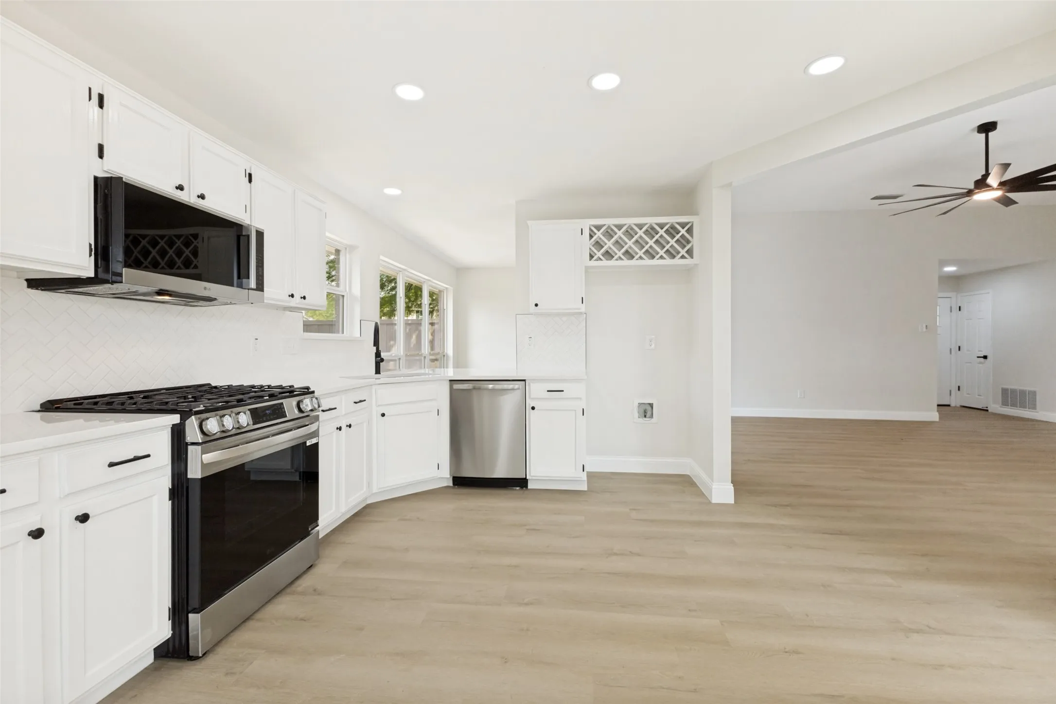 Bright kitchen featuring white cabinetry, stainless steel appliances, light-toned wood-finish flooring, recessed lighting, and an integrated wine rack