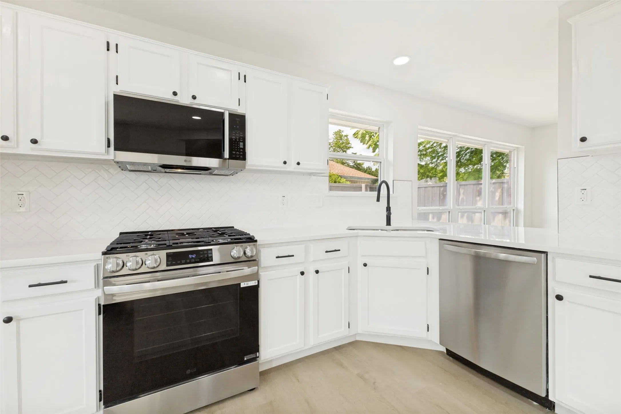 Modern kitchen featuring white cabinetry, stainless steel appliances, a white herringbone tile backsplash, light wood-finish flooring, and white countertops