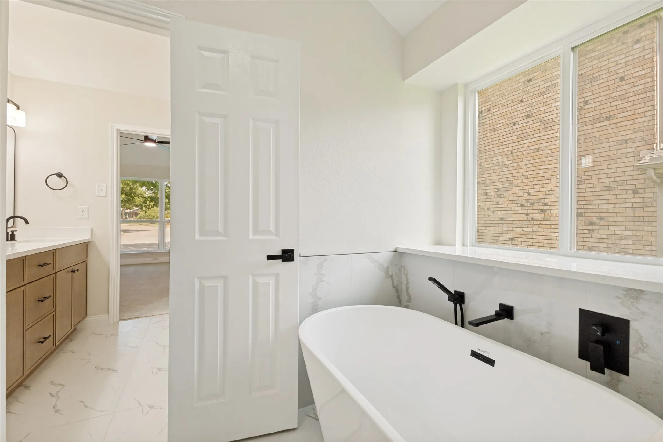 Freestanding soaking tub with matte black fixtures, set against a tiled accent wall and large windows