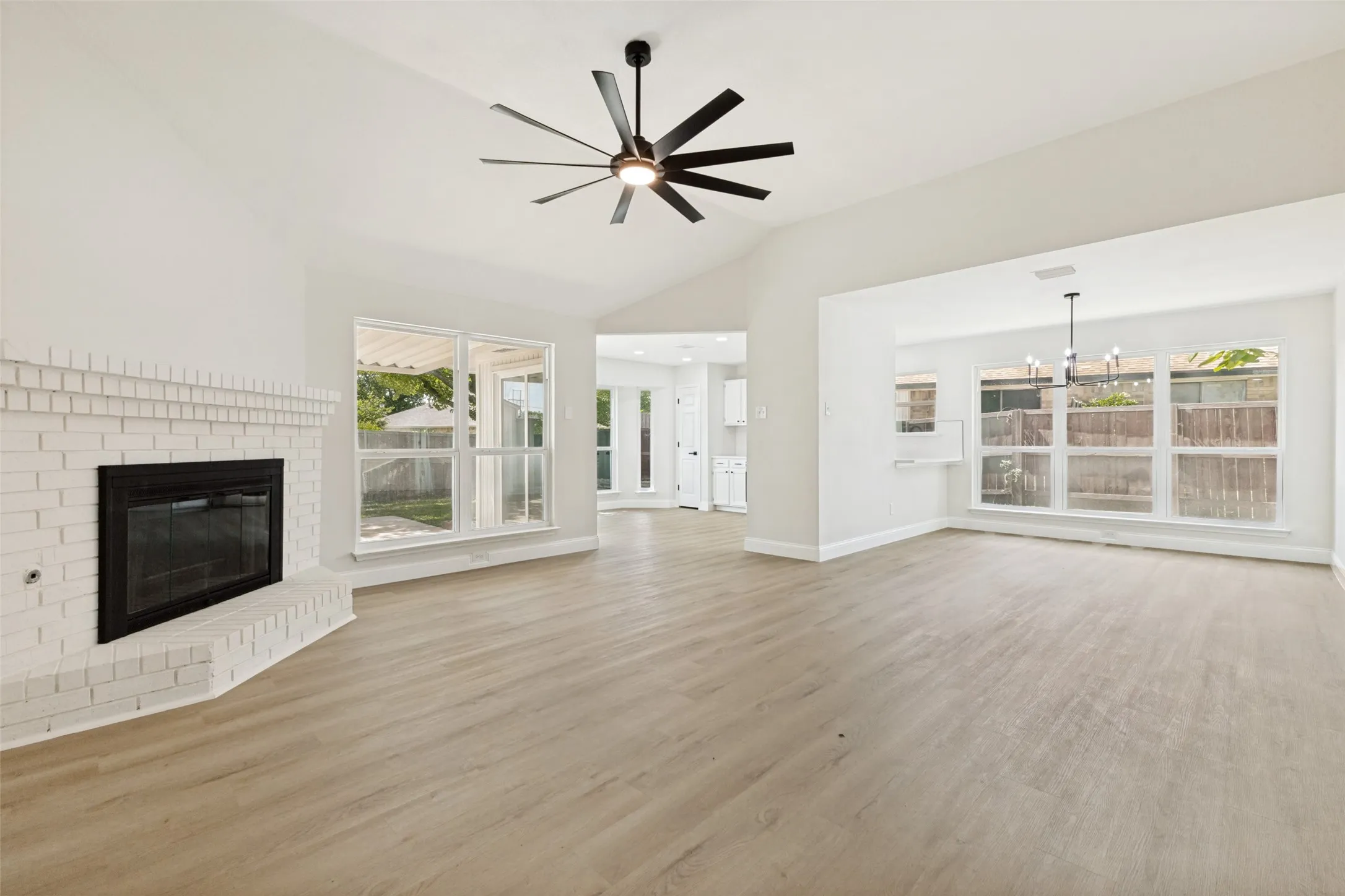 Open concept living area featuring wood-finish flooring, a white brick fireplace, vaulted ceilings, and a modern ceiling fan