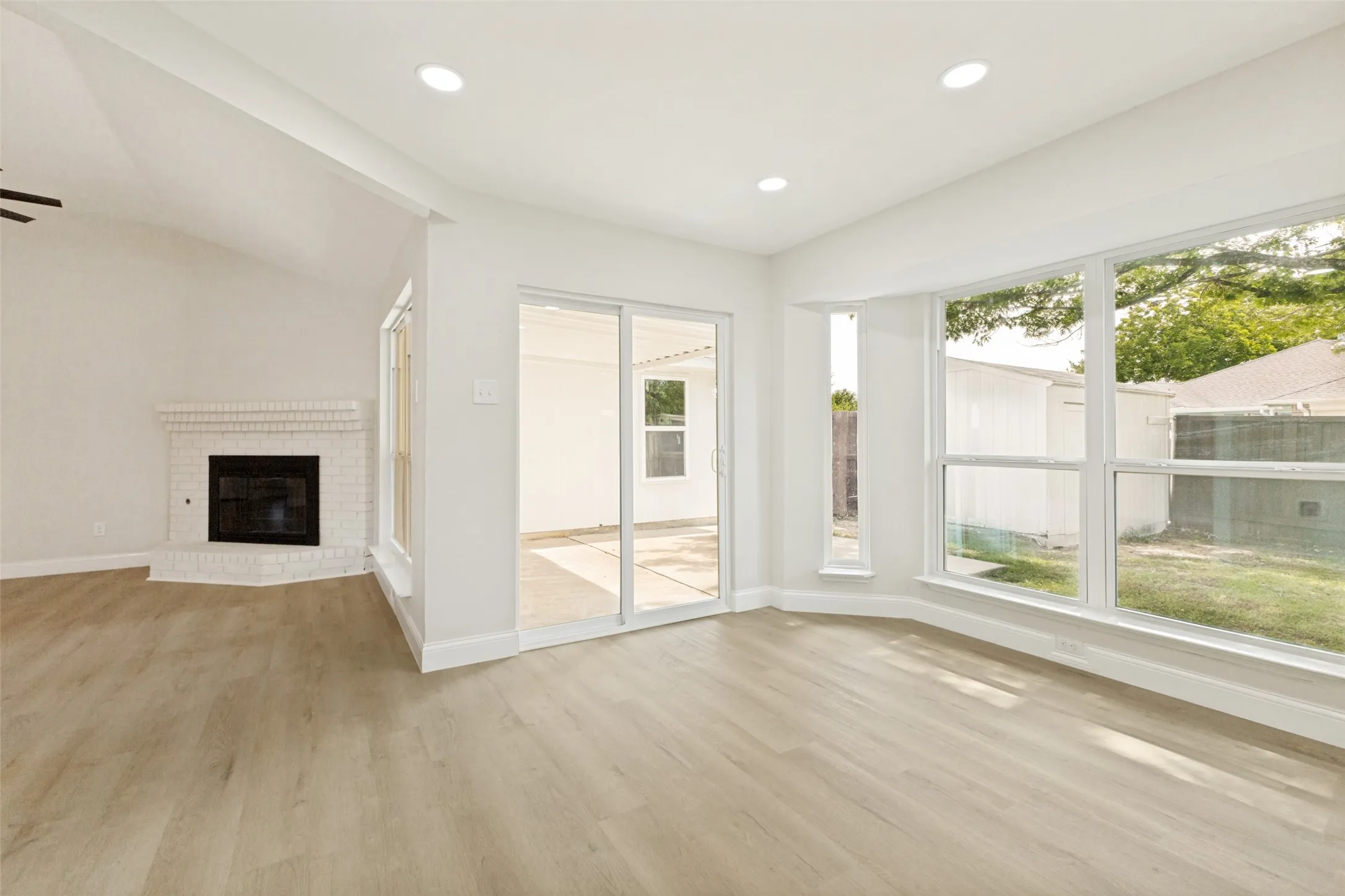 Spacious interior featuring light wood-finish flooring, recessed lighting, and a white brick fireplace