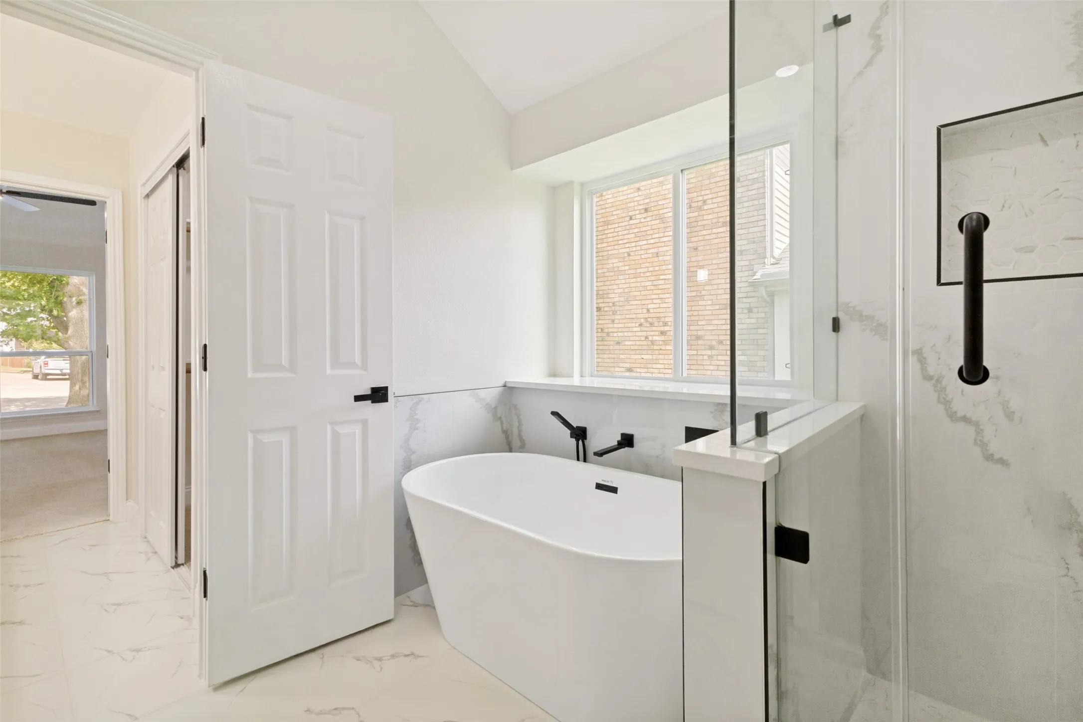 Bathroom featuring a freestanding tub with a wall-mounted faucet, a glass-enclosed shower, and white tile flooring