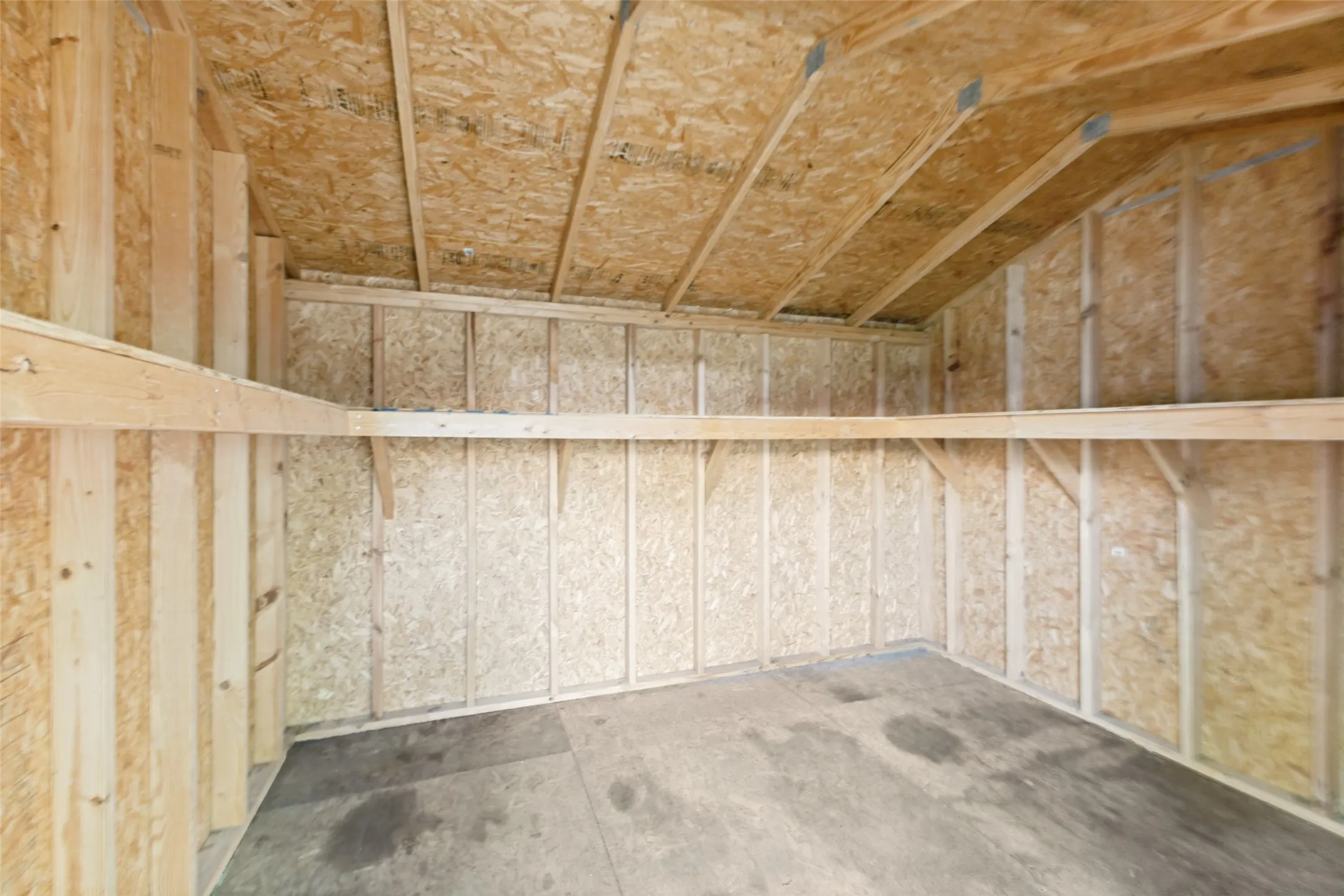 Interior structure featuring wood framing and OSB paneling, concrete flooring, and built-in wood shelving