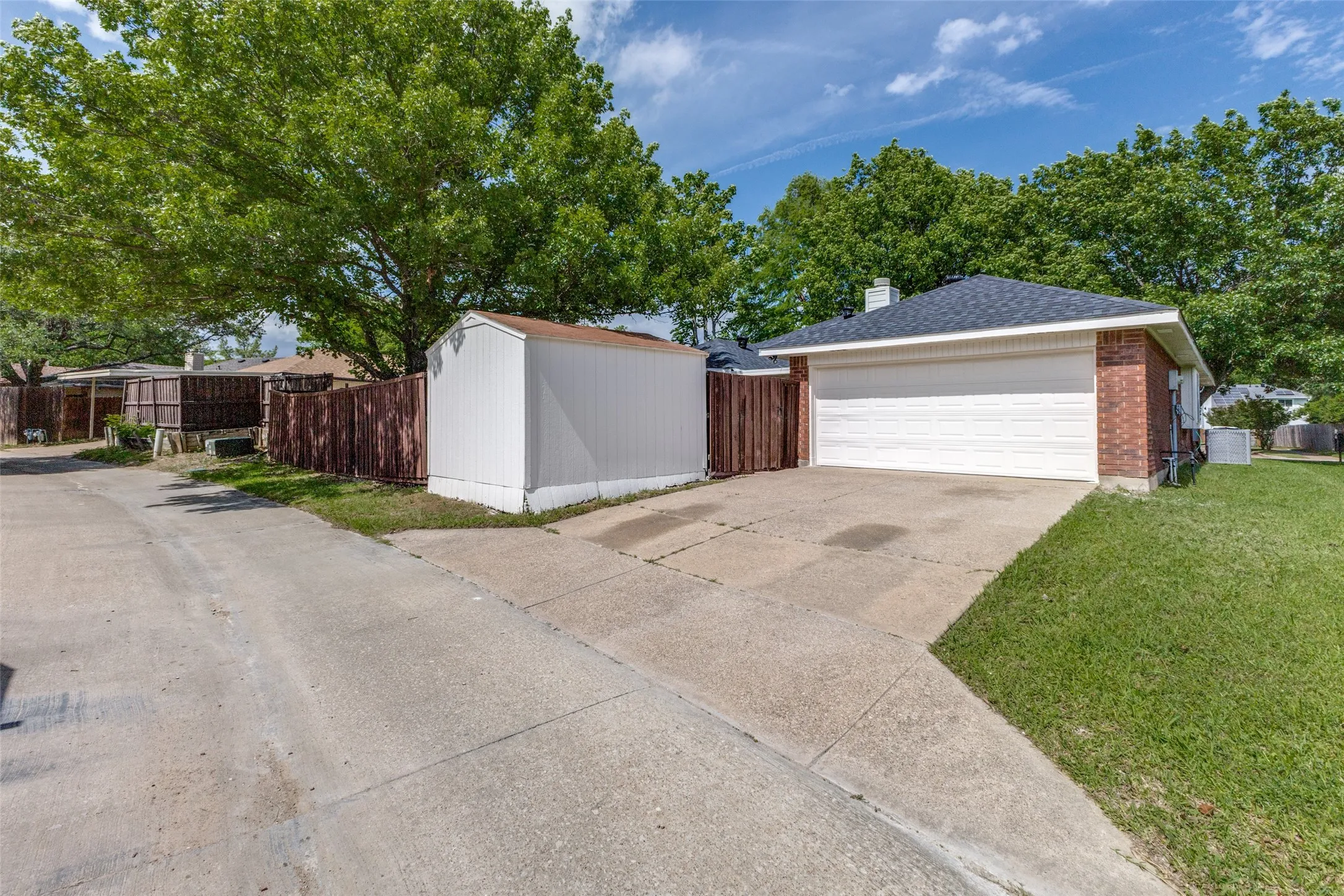 Brick exterior with a white garage door, dark shingle roof, and concrete driveway