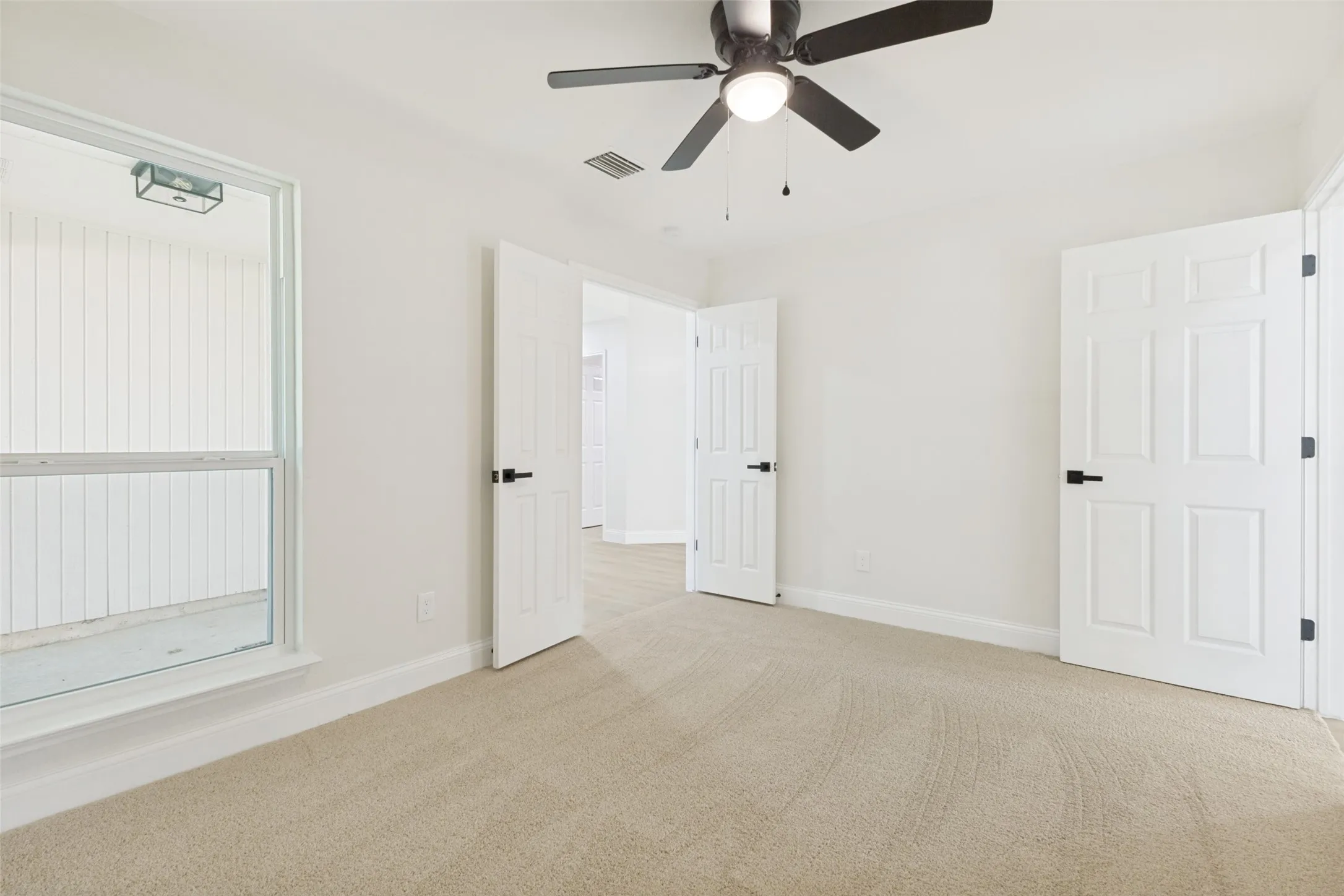 Bright interior space featuring light-toned carpeting, white walls, and a ceiling fan with integrated lighting