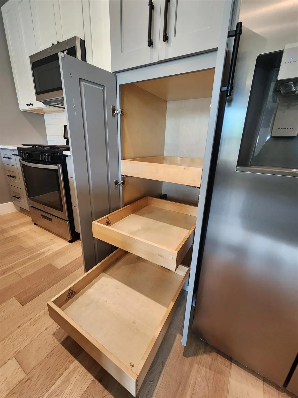 Custom cabinetry with pull-out shelving, stainless steel appliances, wood-finish flooring, and white upper cabinets with matte black hardware