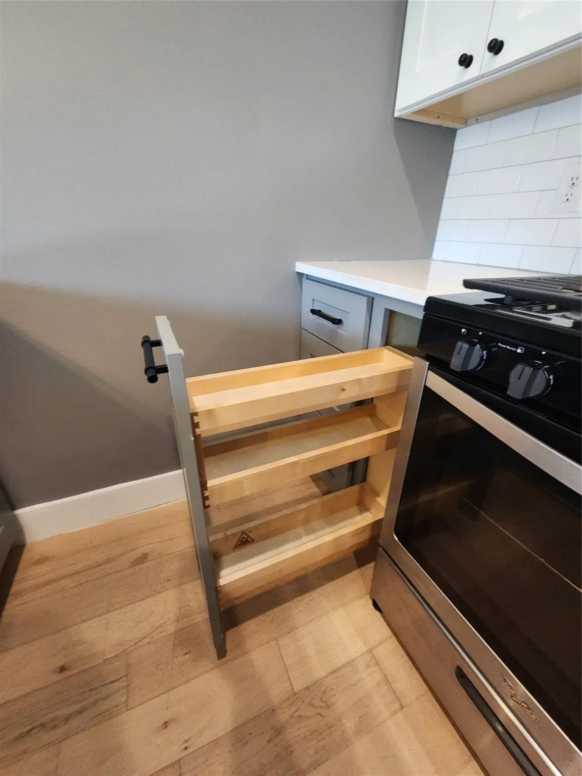 Pull-out spice rack for optimized kitchen storage, quartz countertop, white subway tile backsplash, stainless steel range, and wood-finish flooring