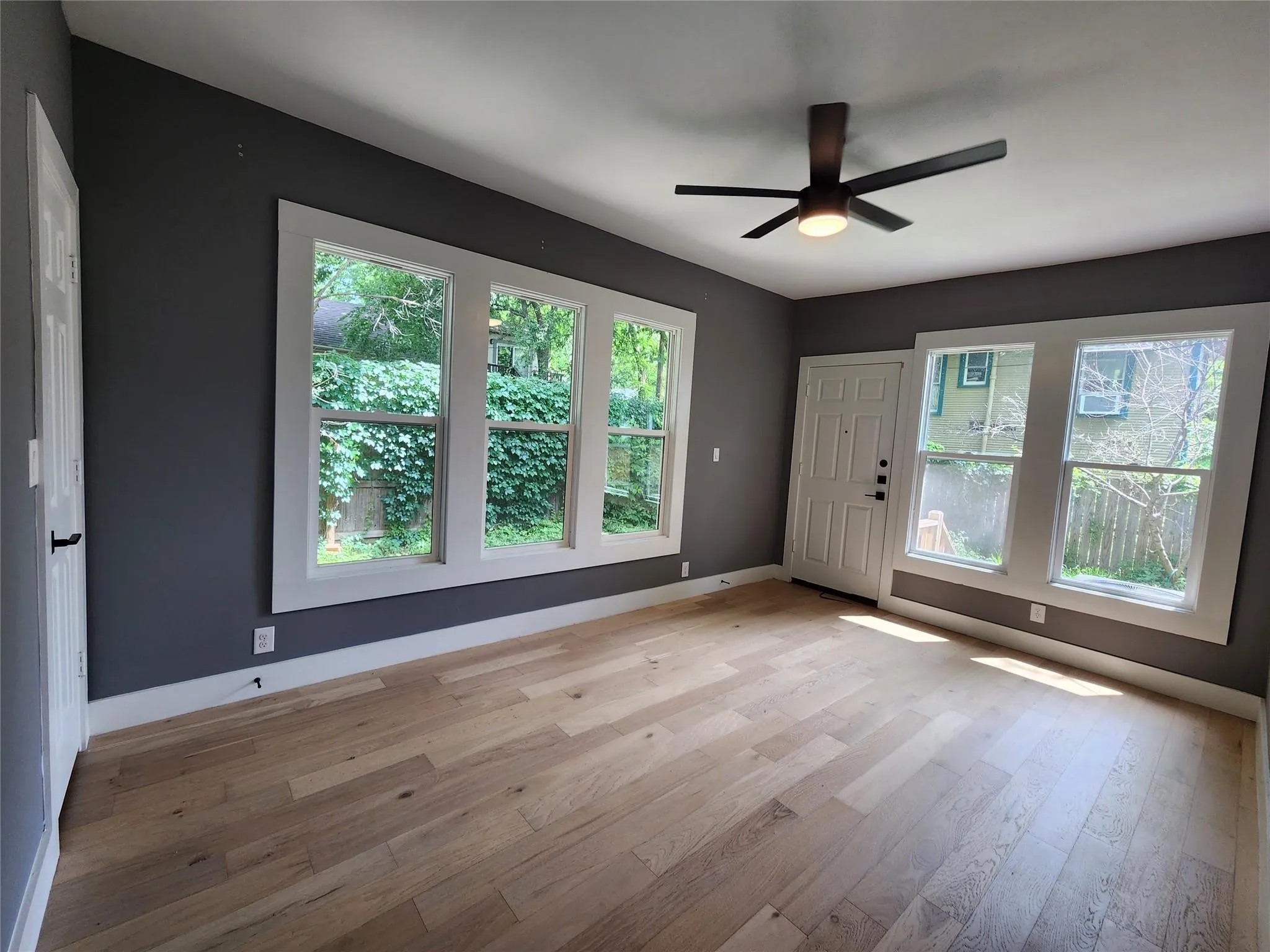 Spacious room featuring light wood-finish flooring, dark grey walls, and white trim