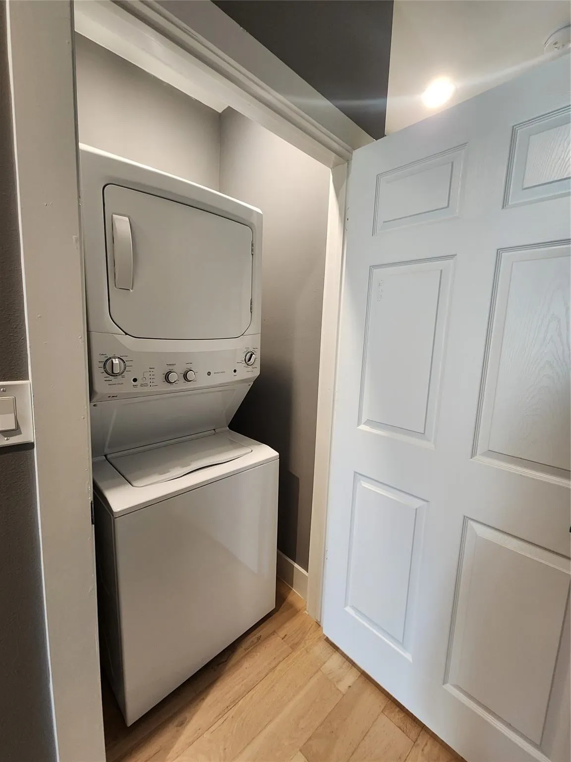 Dedicated laundry closet featuring a stacked washer and dryer, wood-finish flooring, and a six-panel door
