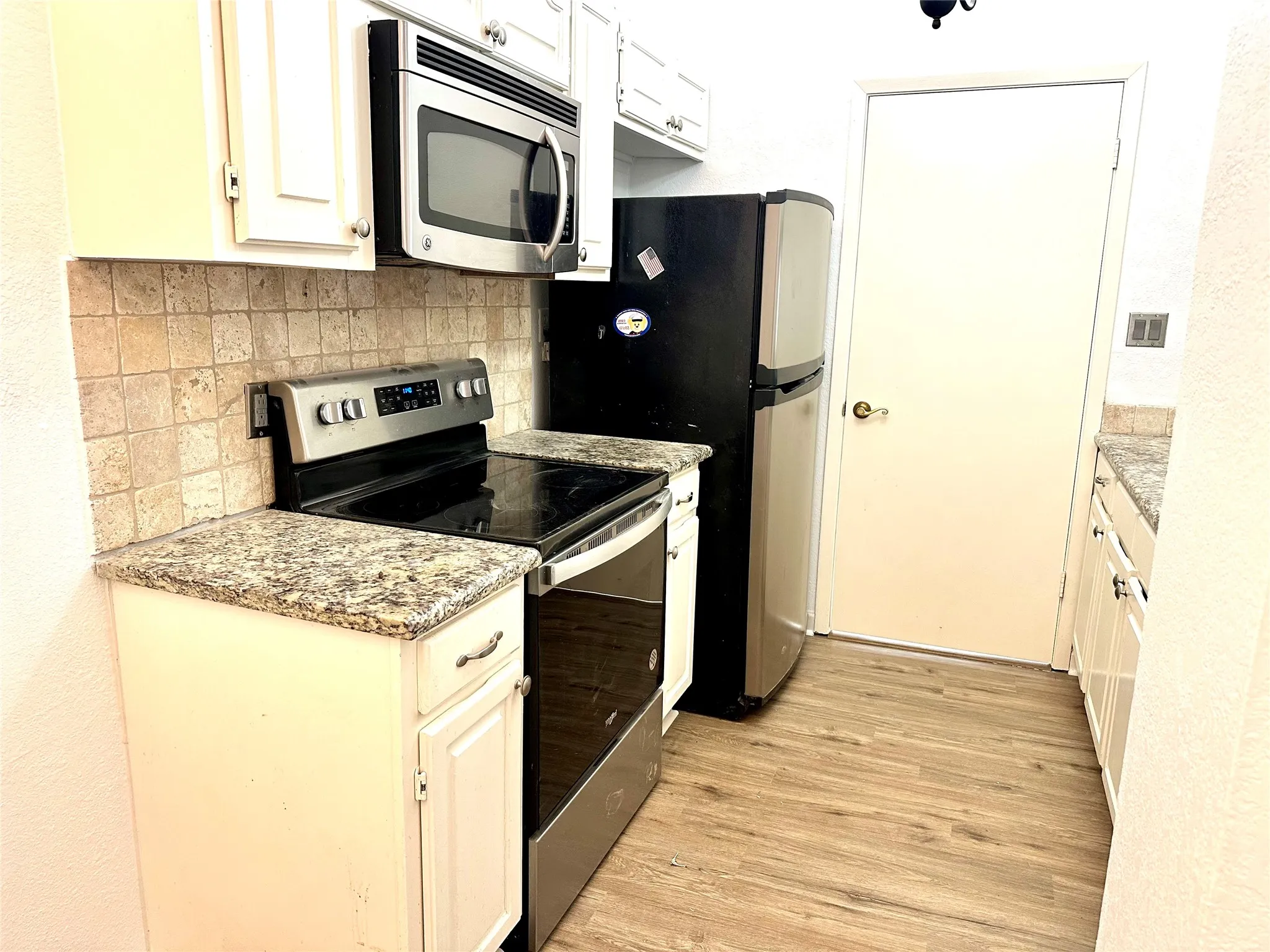 Kitchen with light wood-type flooring, stainless steel appliances, decorative backsplash, and white cabinetry