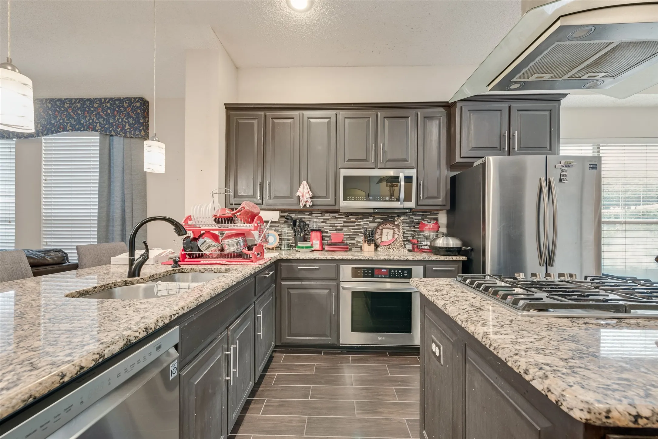 Kitchen featuring granite countertops, wood-finish flooring, dark cabinetry, and stainless steel appliances including a built-in oven, microwave, and gas cooktop