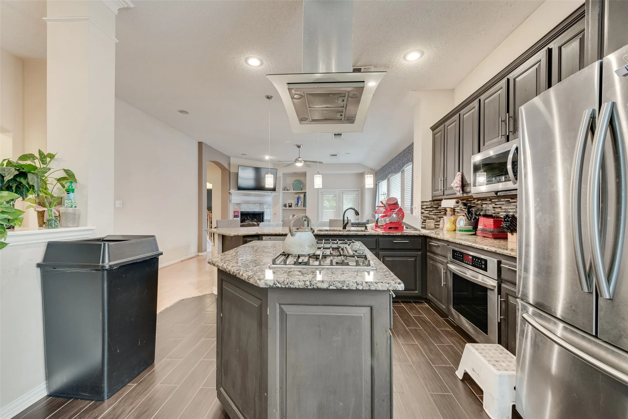 Kitchen featuring a central island with a gas cooktop, granite countertops, wood-finish flooring, stainless steel appliances, and dark cabinetry