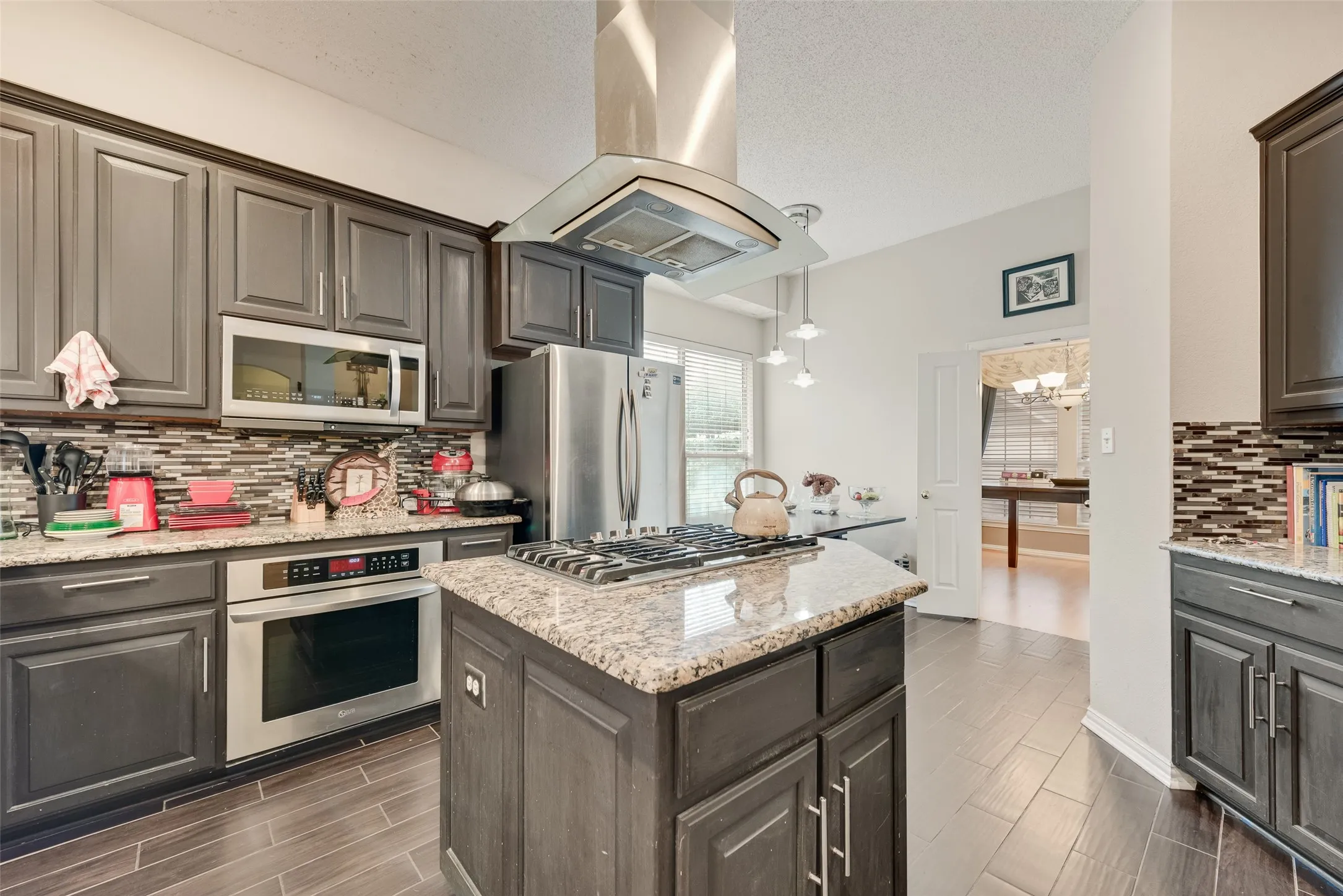 Kitchen featuring a central island with a gas cooktop, granite countertops, wood-finish flooring, stainless steel appliances, and dark shaker-style cabinetry