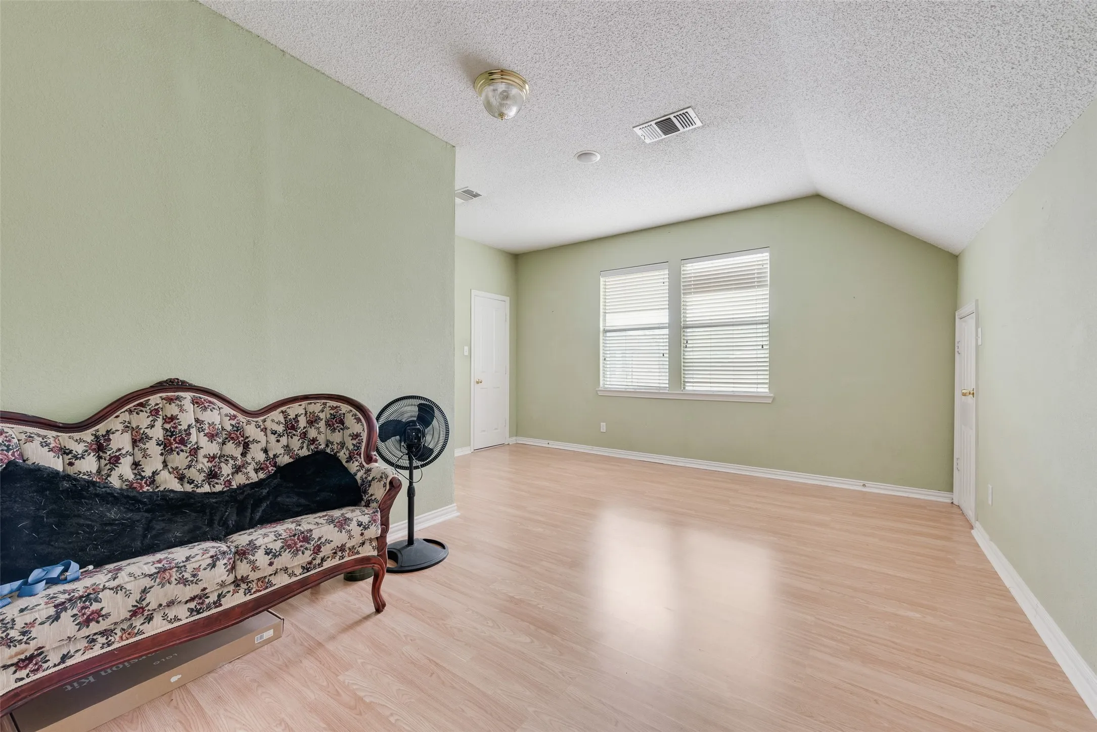 Spacious room featuring wood-finish flooring, vaulted ceilings, and two windows with blinds
