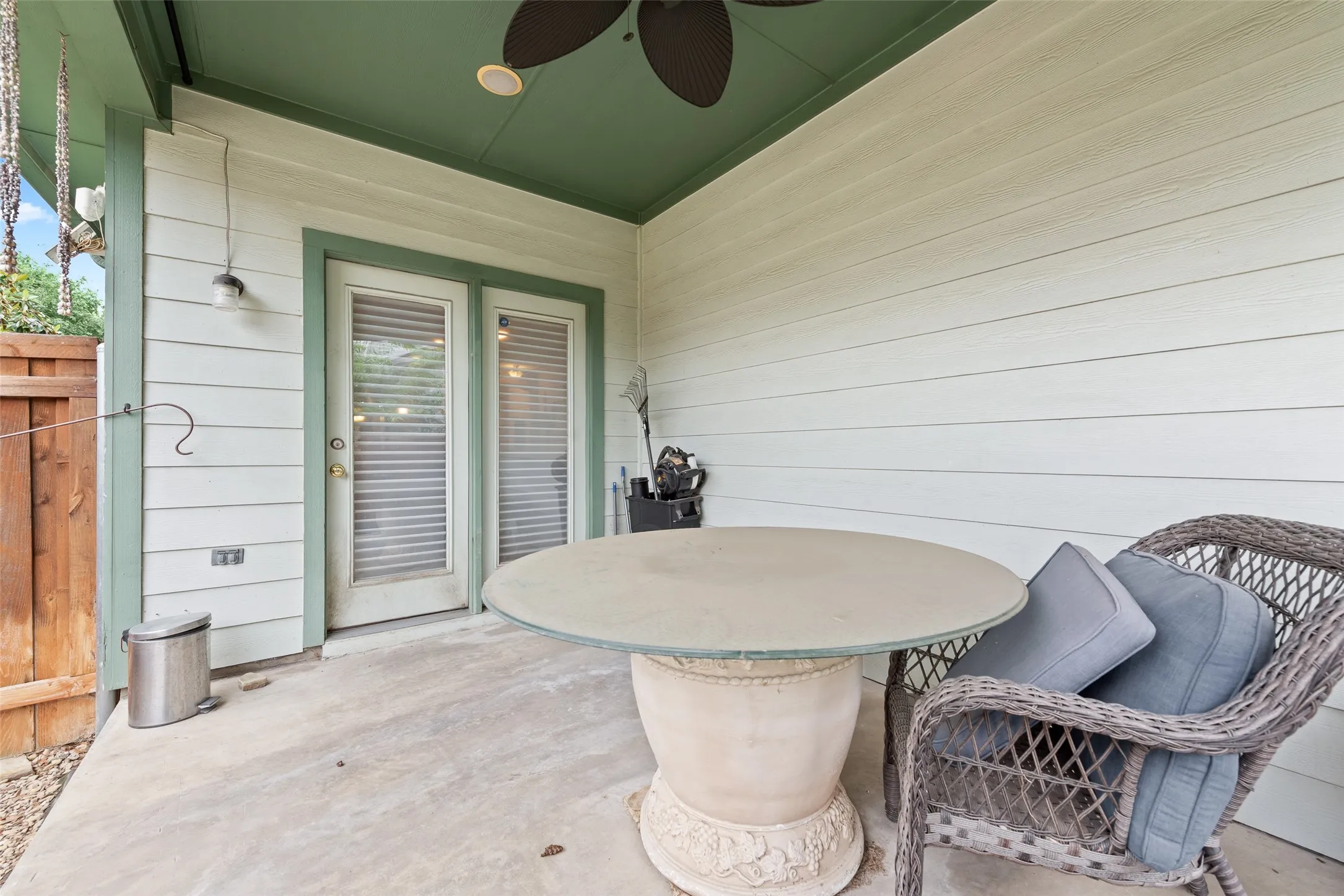 Covered patio featuring a ceiling fan, concrete flooring, double glass panel doors, siding exterior, and a wood fence