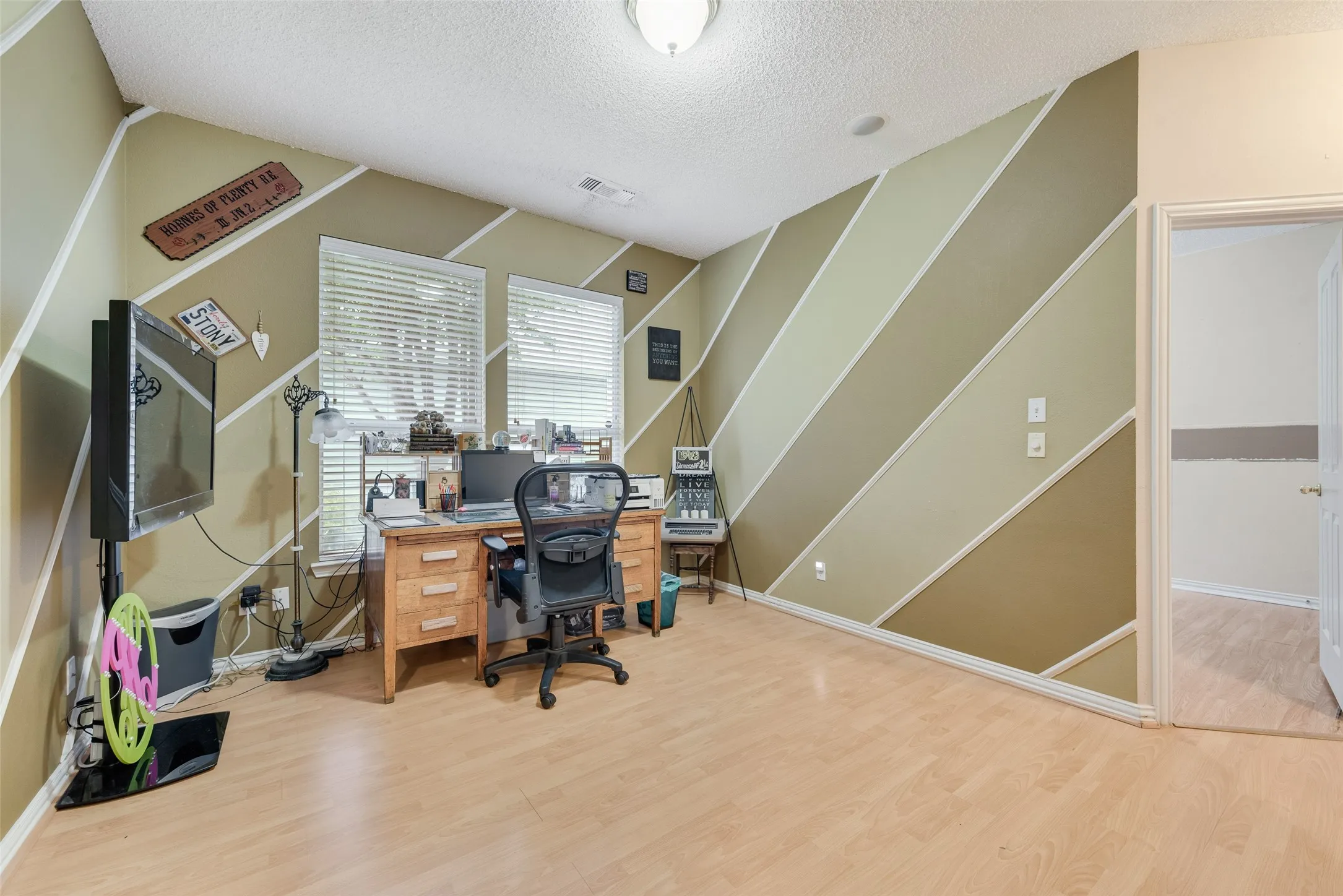 Room featuring light wood-finish flooring, textured white ceiling, and dual windows with blinds