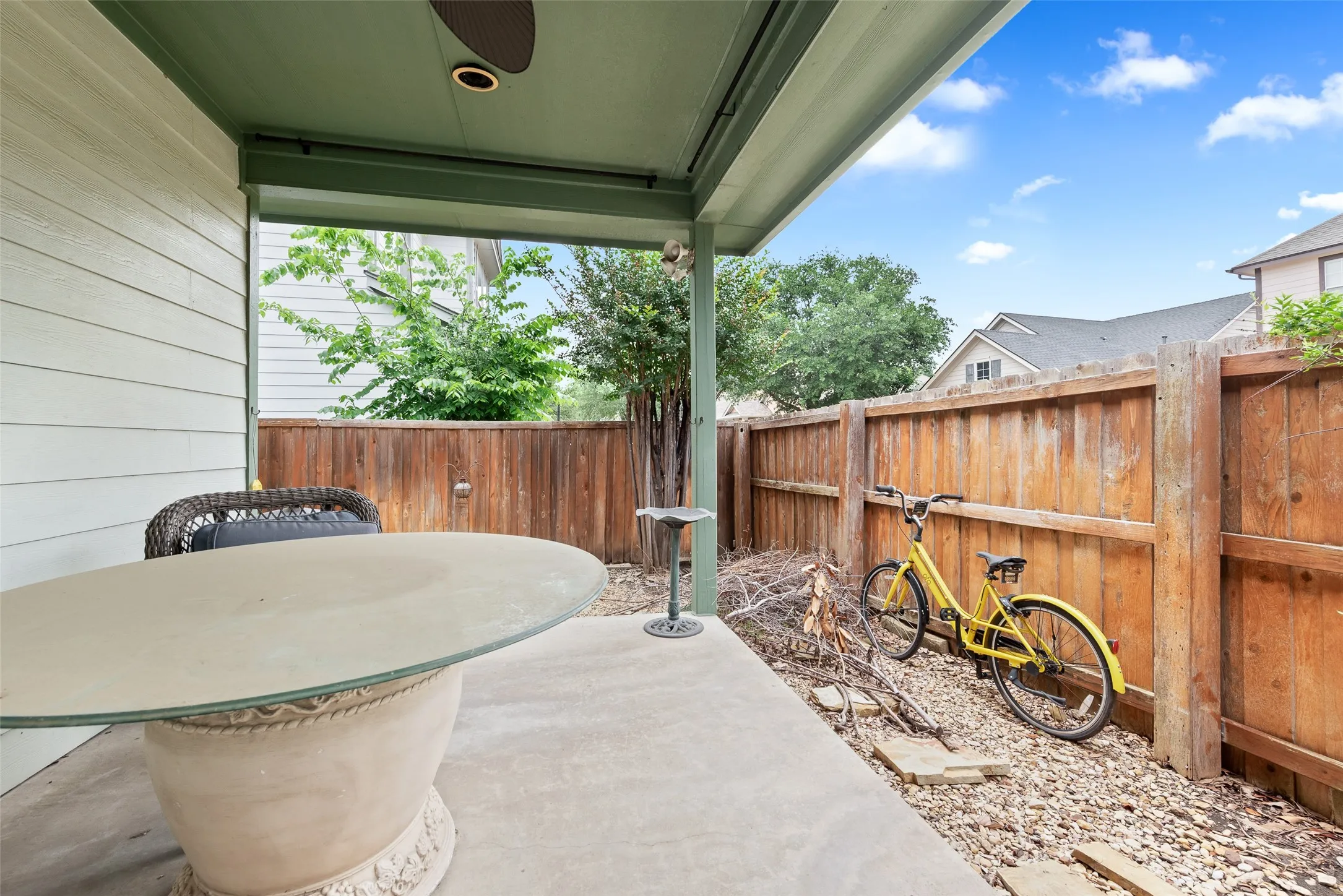 Covered patio featuring concrete flooring, a ceiling fan with integrated lighting, and direct access to an enclosed backyard space with a wood fence and gravel landscaping