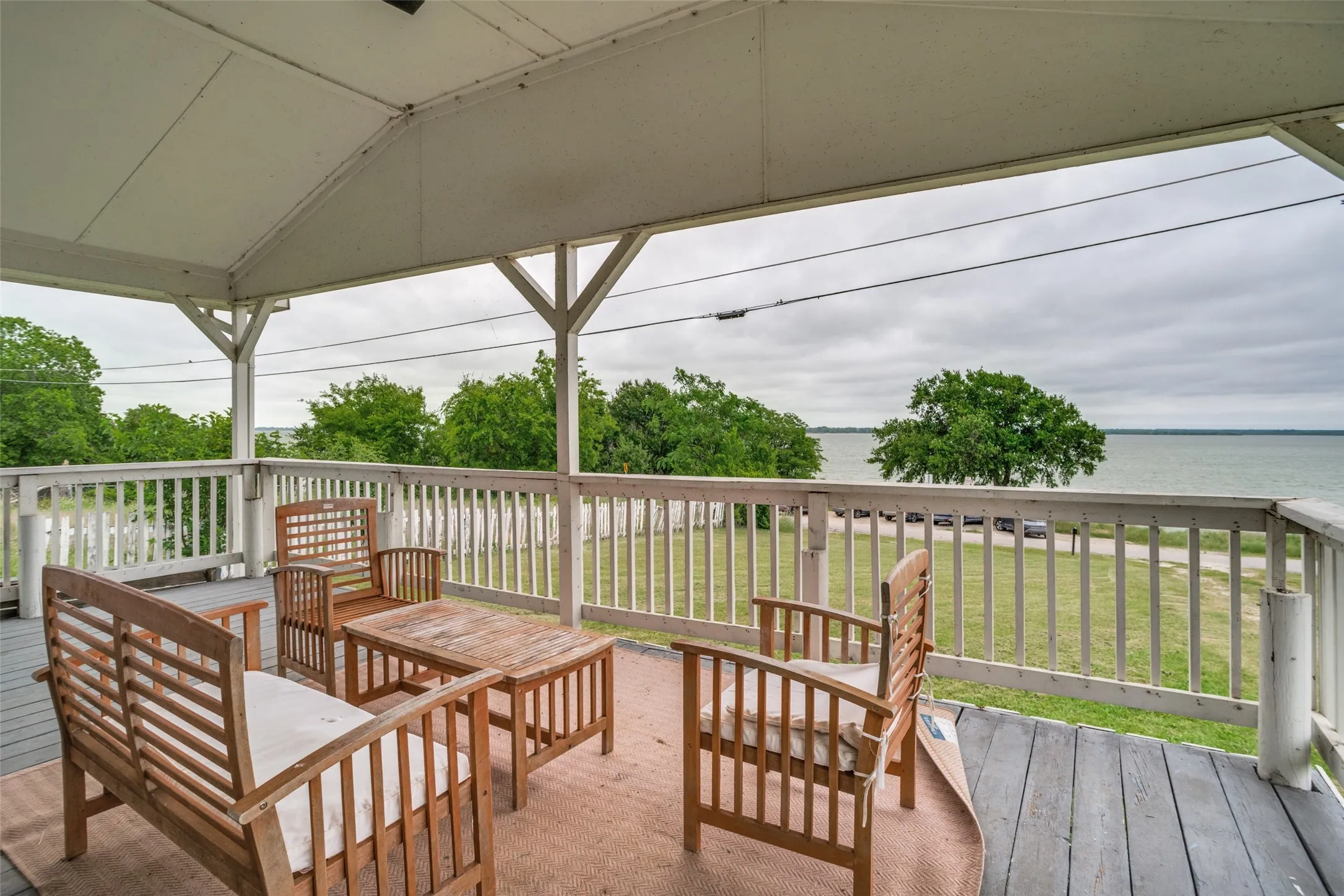 Covered outdoor deck featuring white painted railings and a water backdrop