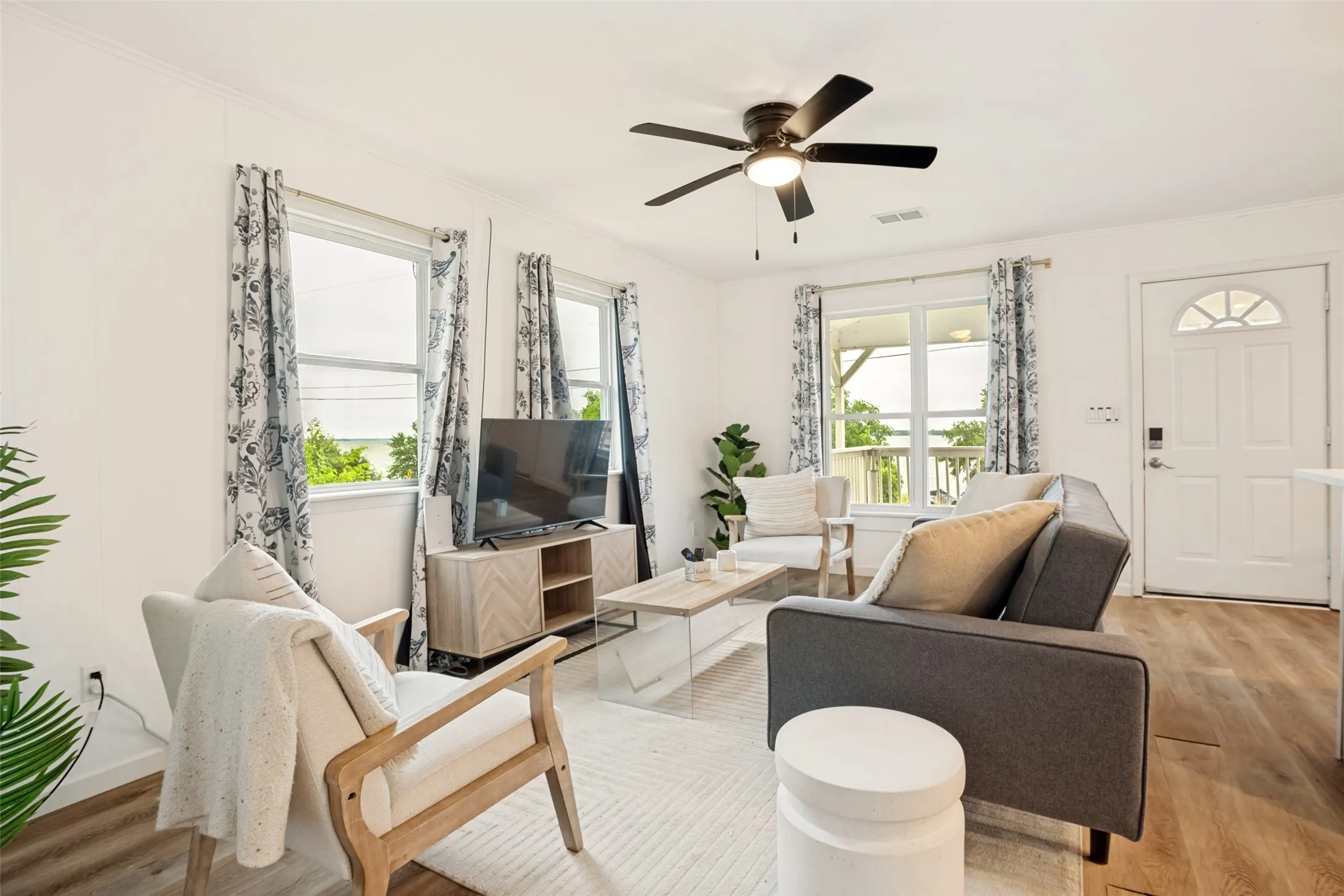 Bright living area featuring wood-finish flooring, a ceiling fan with light, and multiple windows