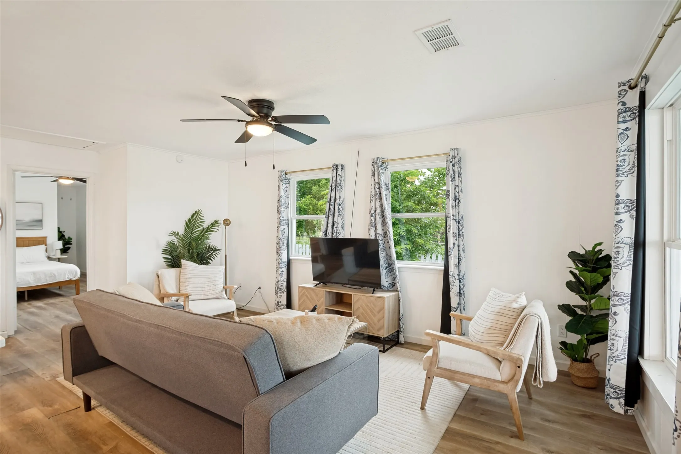 Spacious living area featuring wood-finish flooring, a ceiling fan, and ample natural light from multiple windows