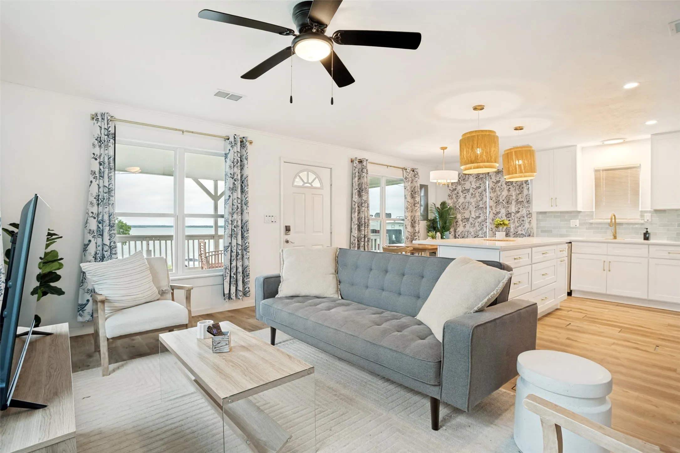 Open-concept living area featuring wood-finish flooring, a contemporary ceiling fan, and a kitchen with white cabinetry and a backsplash