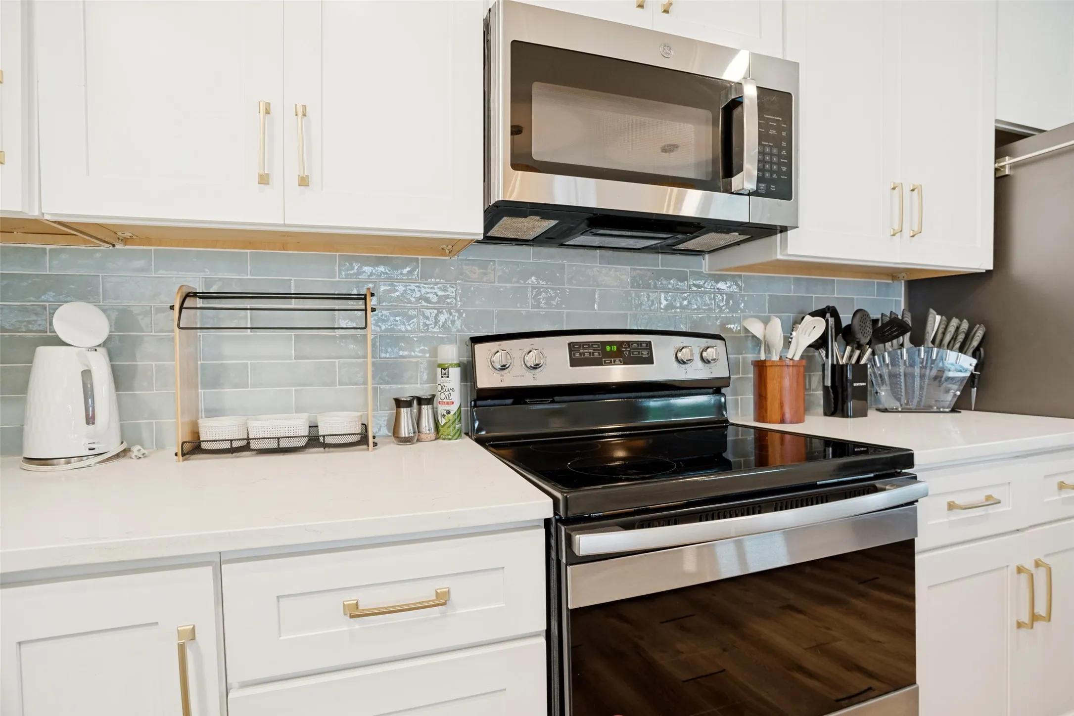 Modern kitchen featuring white cabinetry with gold-tone hardware, a tiled backsplash, solid surface countertops, and stainless steel appliances