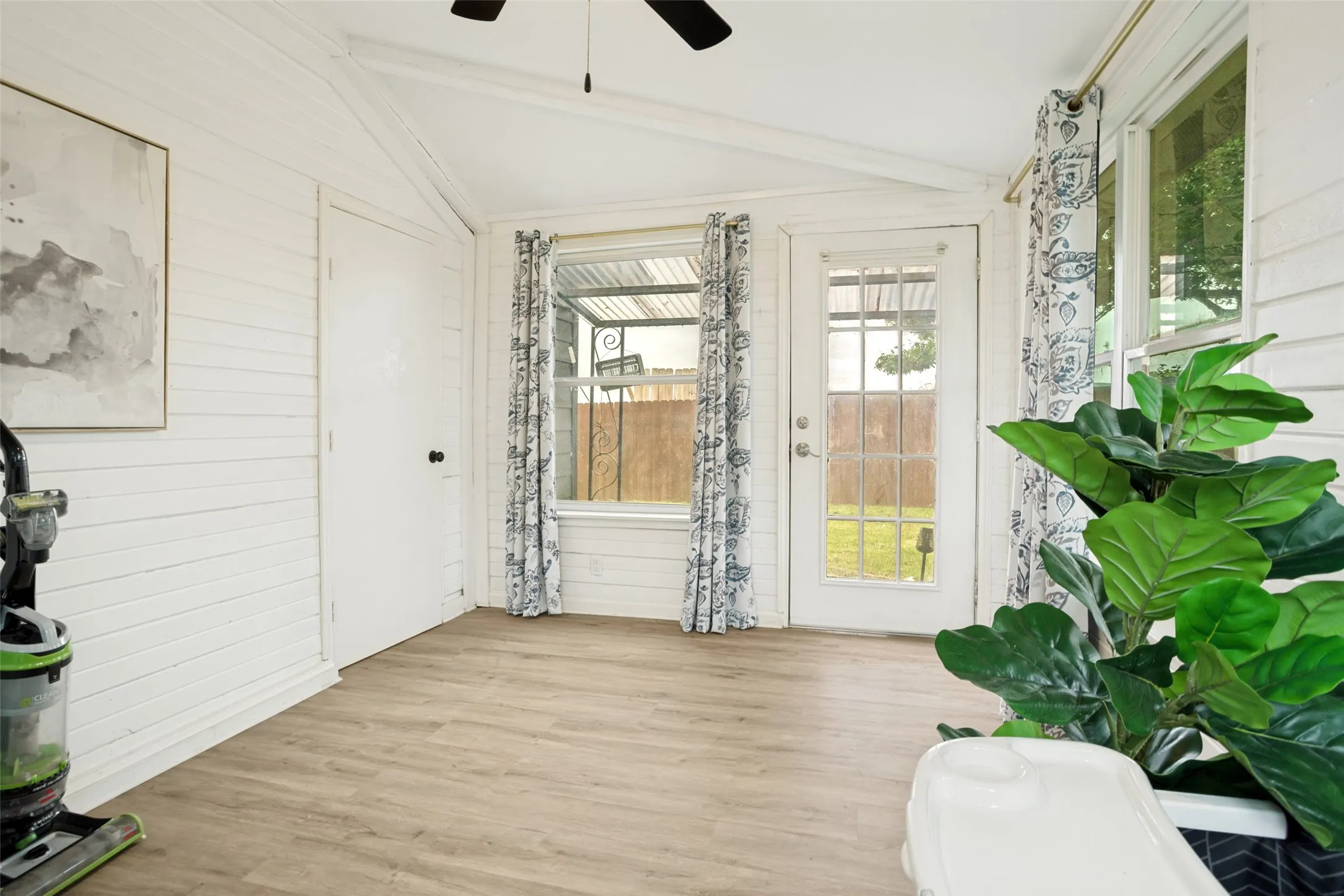 Sunroom featuring white shiplap walls, wood-finish flooring, a ceiling fan, and a glass-paned exterior door