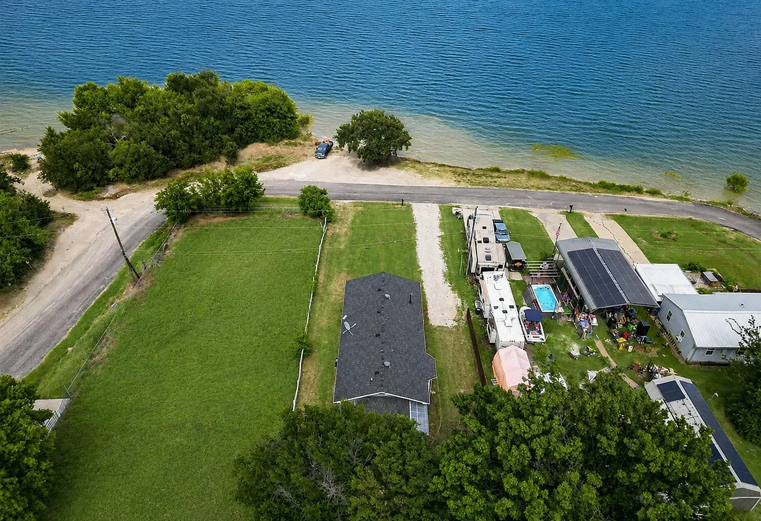 Expansive green space bordering a body of water, featuring a gravel road and mature trees
