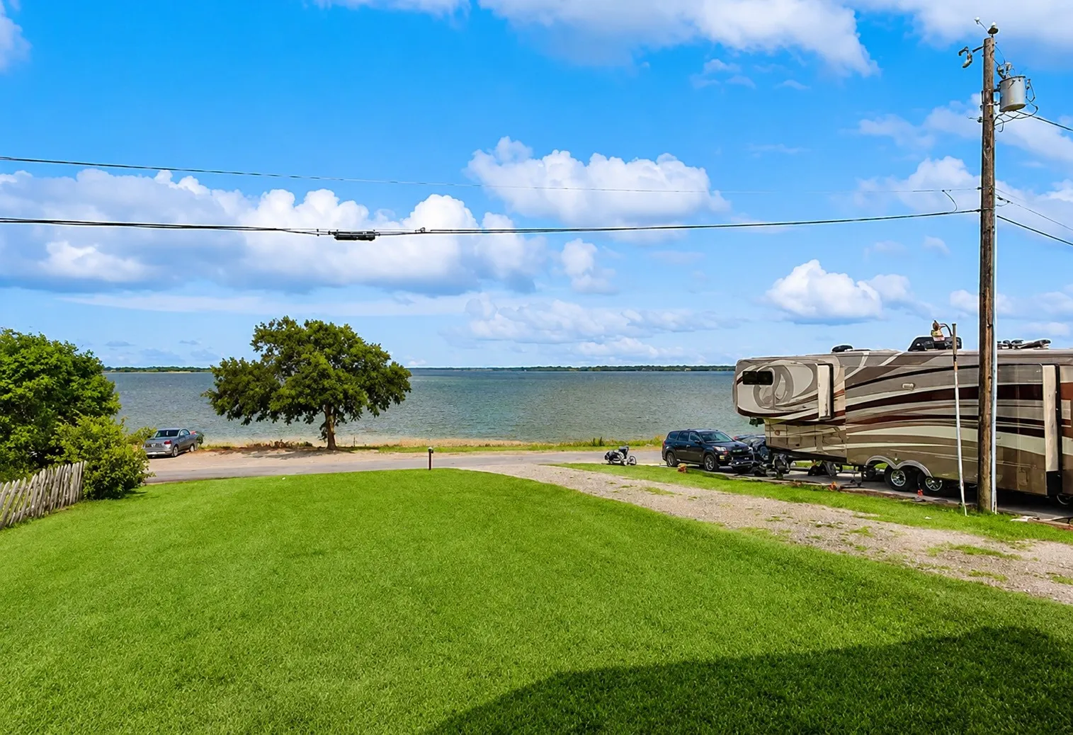 Expansive waterfront property featuring a manicured lawn, mature trees, and a gravel driveway