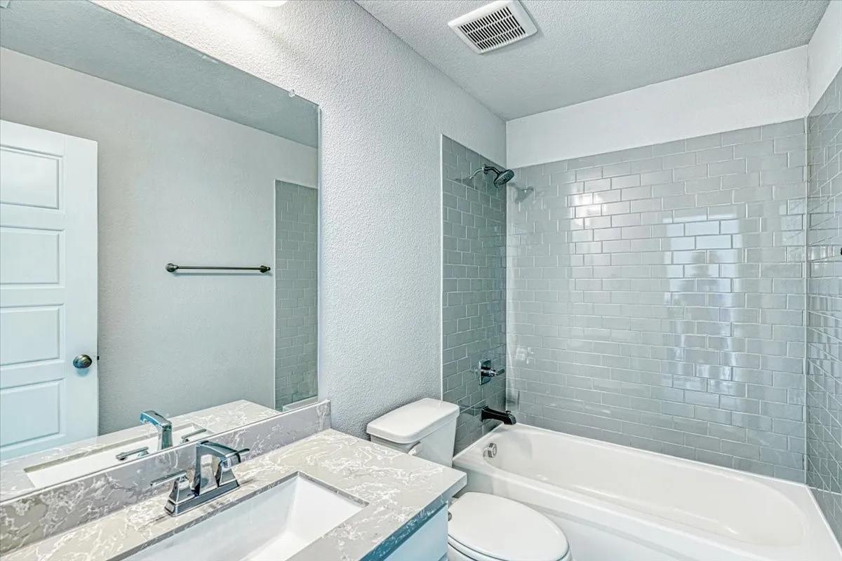 Full bathroom with a textured ceiling, toilet, tiled shower / bath combo, and large vanity