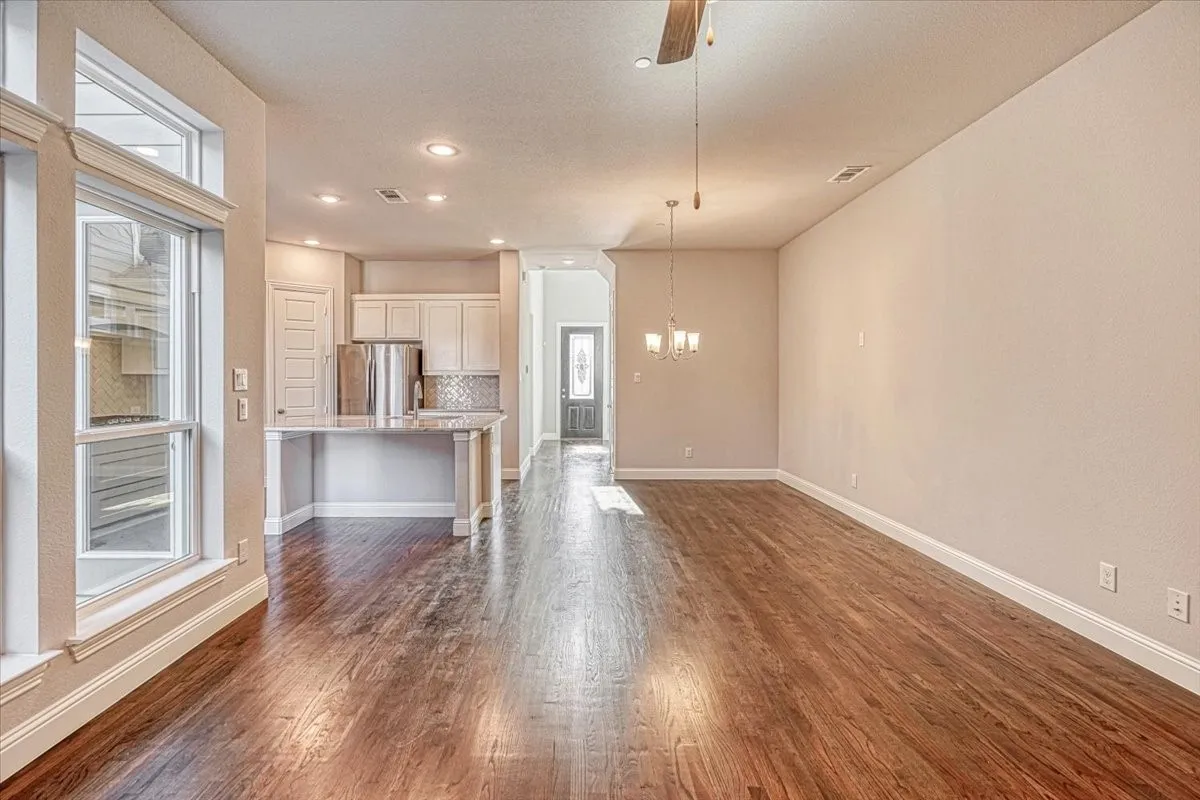 Unfurnished living room featuring dark wood-type flooring and ceiling fan with notable chandelier
