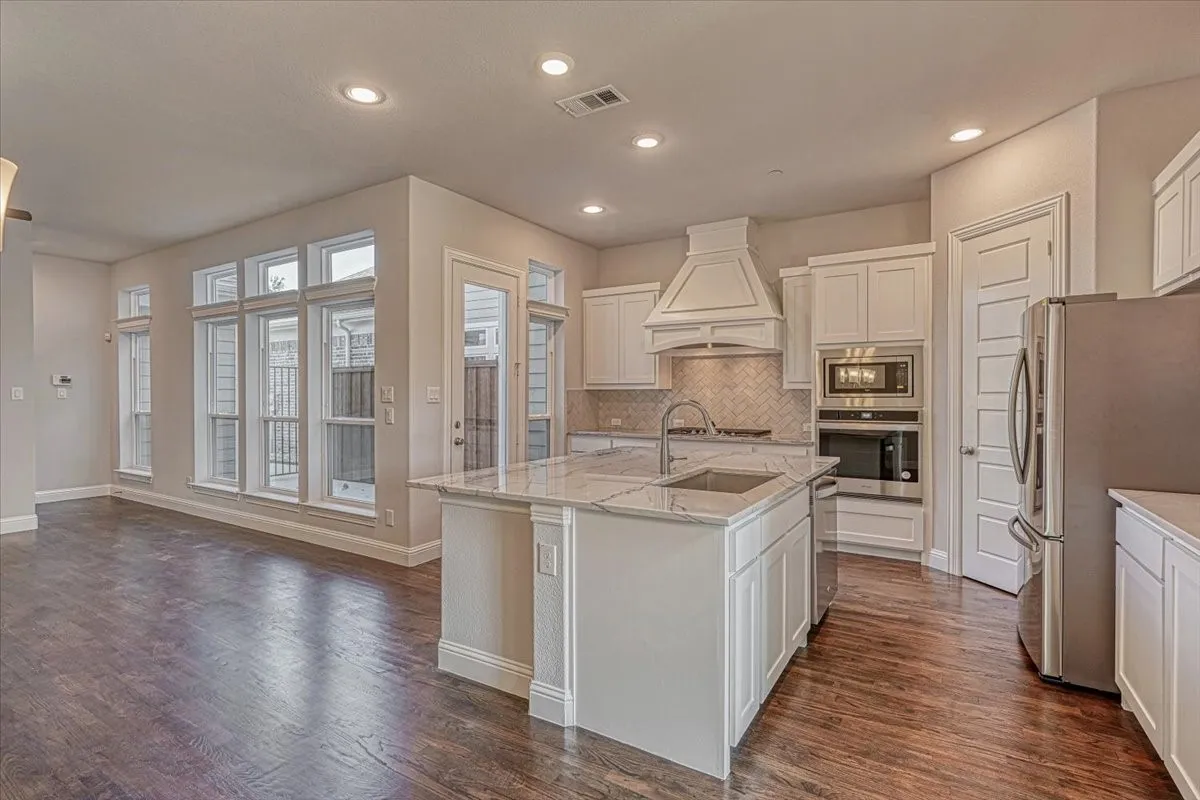 Kitchen with dark hardwood / wood-style floors, a center island with sink, white cabinetry, appliances with stainless steel finishes, and premium range hood