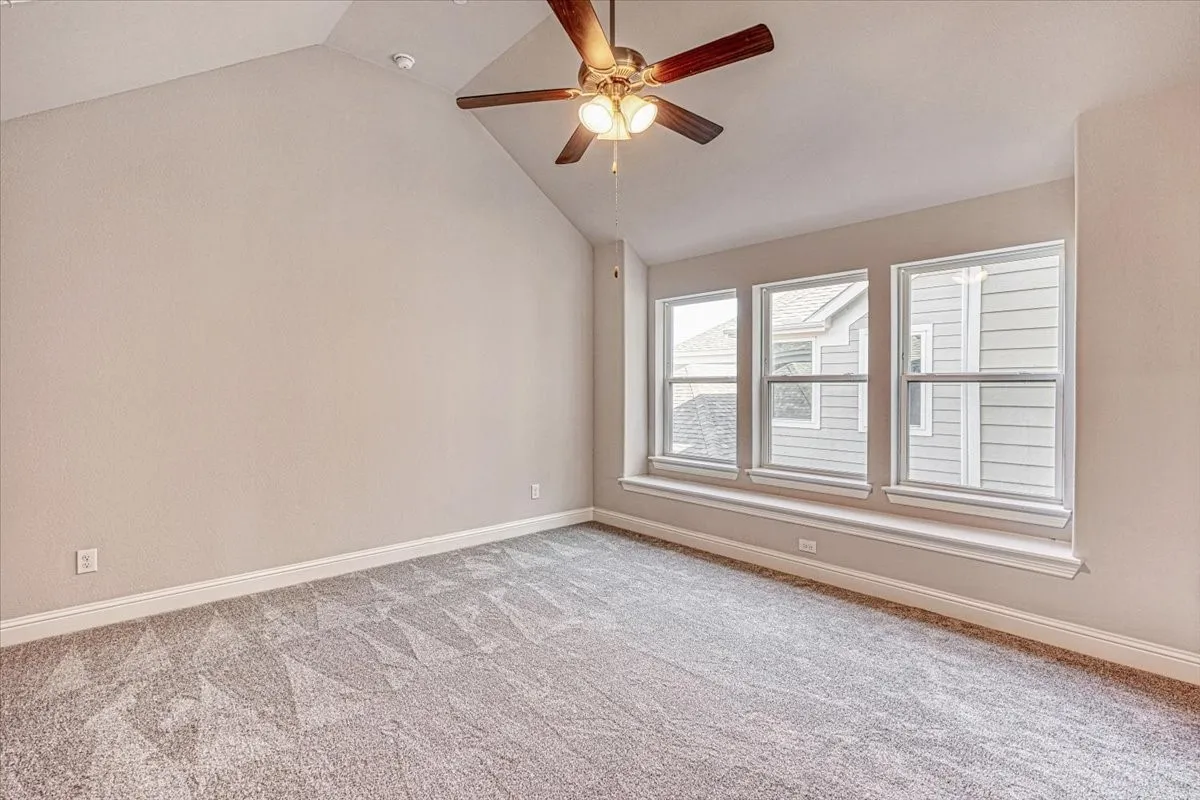 Carpeted empty room with ceiling fan and vaulted ceiling