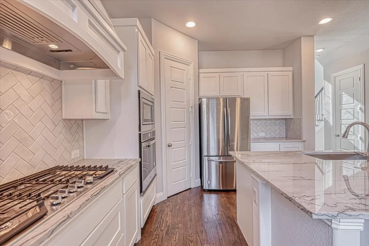Kitchen with dark hardwood / wood-style flooring, backsplash, white cabinetry, appliances with stainless steel finishes, and premium range hood